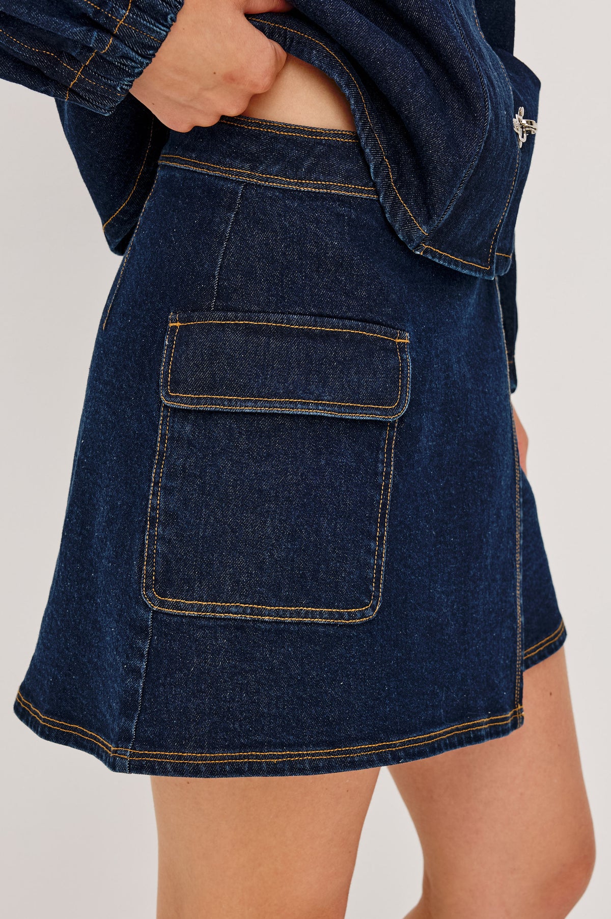 Dillon Mini Skirt in Midweight Denim With Mid-Rise, Asymmetric Wrap Design, Toggle Closure at Side Waist, Contrast Topstitching, and Utility Patch Pocket in Rinse Indigo Colorway - Lower Body Front View Featured on Model