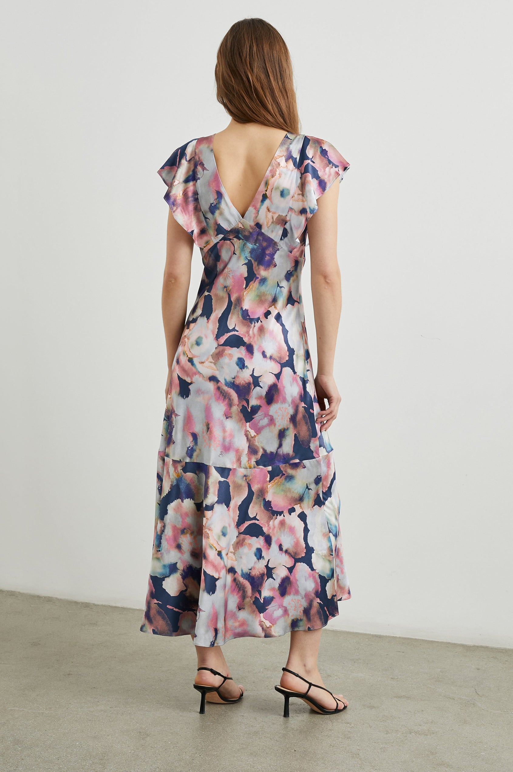 Dina Short-Sleeve Midi Dress with a Deep V Neck, Flutter Sleeves, and a Thigh Side Slit in Midnight Verbena Colorway, Flowers in Pinks, Blues, Oranges and white on Midnight - Back Full Body View Featured on Model