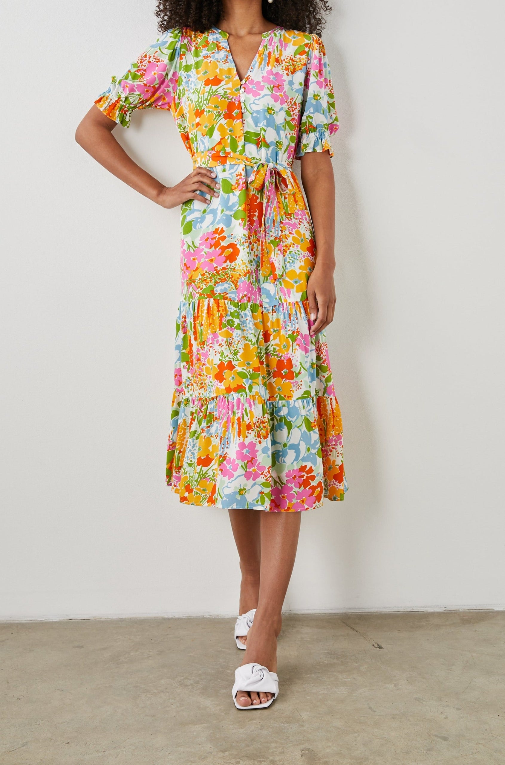 Eliana Midi Dress with Elbow-Length Sleeves with Shirred Cuffs, a V Neck, Buttons Down the Bodice, a Fabric Tie at the Waist  and a Tiered Skirt in Day Garden Colorway, a Floral Pattern in Blue, Pink and Oranges on White - Front Full Body View Featured on Model