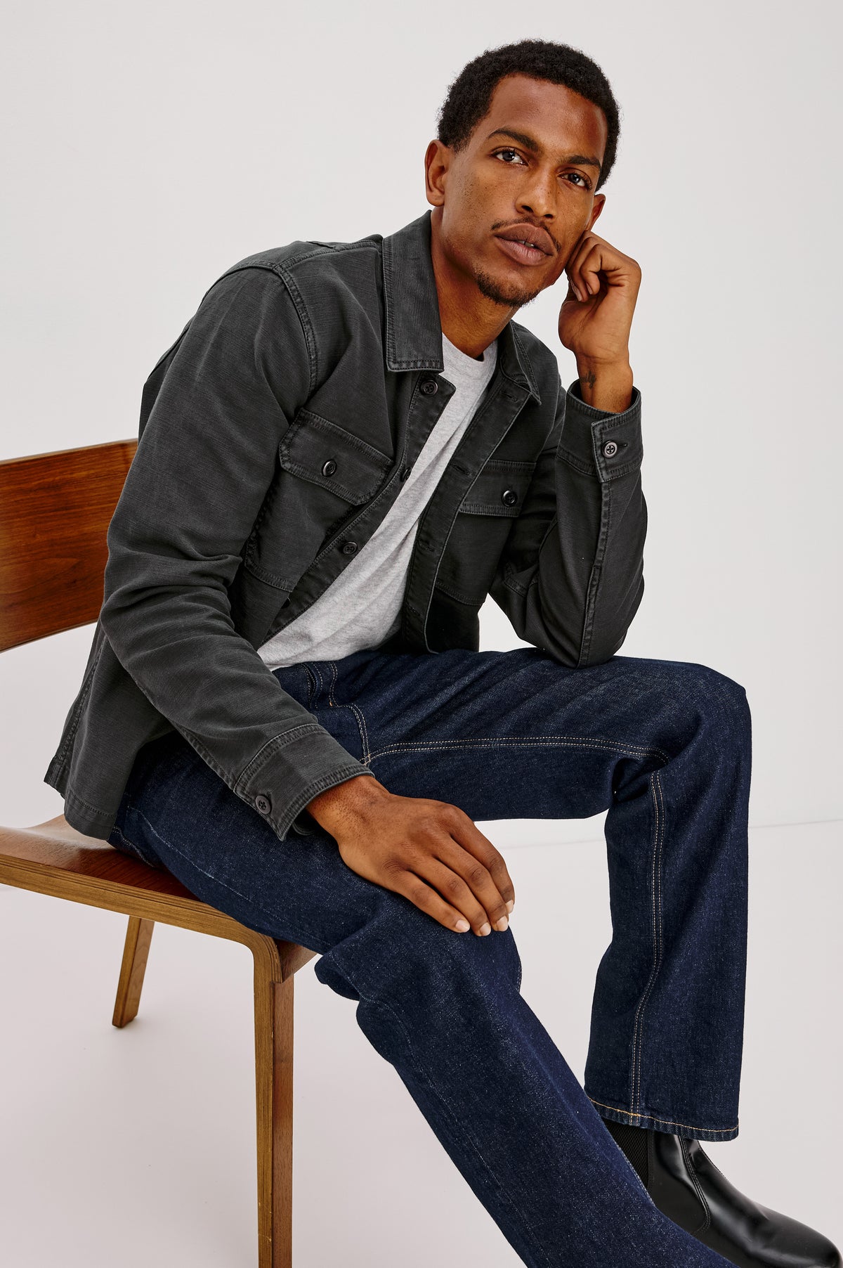 Eliot Shirt With Collar, Chest Buttoned Flap Pockets, Front Buttons, and Long Sleeves in Washed Black Colorway - Full Body View Featured on Model Sitting