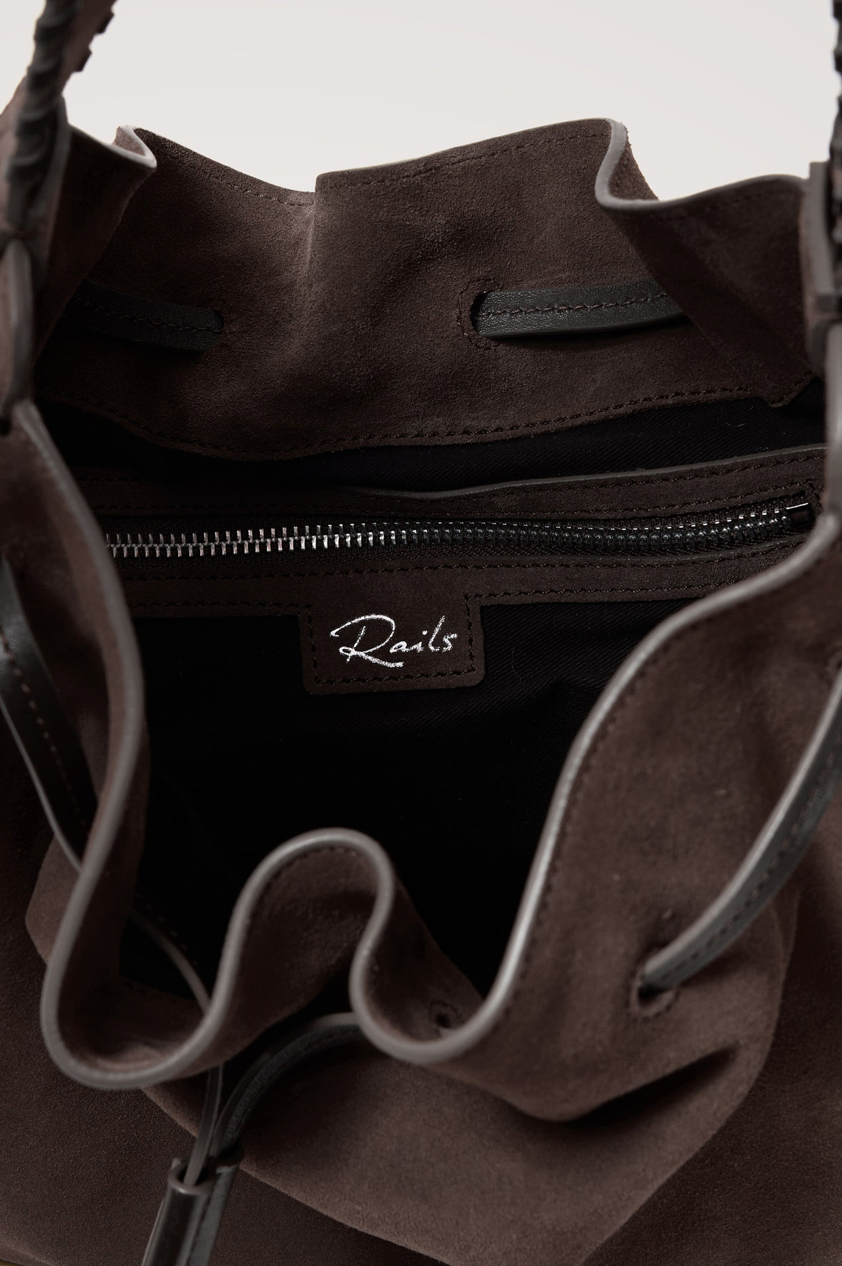 Firenze Bucket Bag in Suede With Whipstitch Trim, Drawcord Closure, and Interior Zip Pocket in Dark Brown Suede Colorway - close up view of interior showing rails logo on the interior pocket.