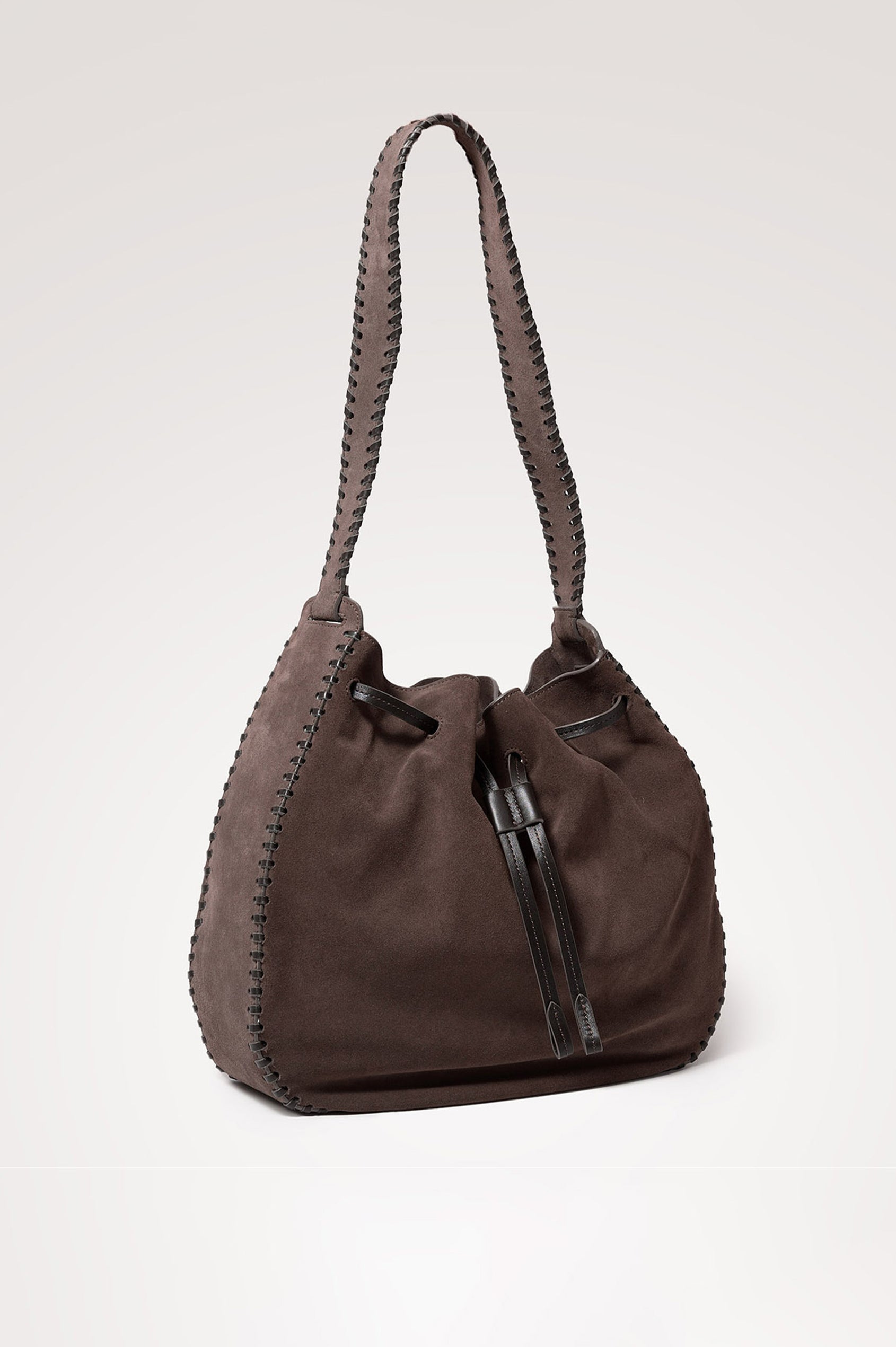 Firenze Bucket Bag in Suede With Whipstitch Trim, Drawcord Closure, and Interior Zip Pocket in Dark Brown Suede Colorway - front 3/4 view of bag with strap extended.