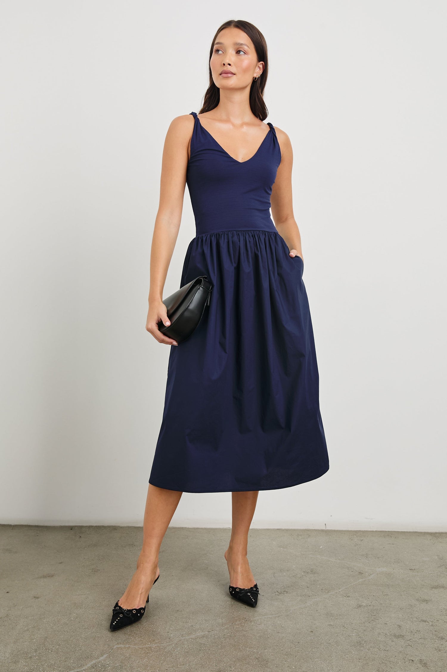 Franca Sleeveless Midi Dress with Twisted Shoulder Straps, a deep V Neck and Pleats at the Waist in Navy Colorway - Front Full Body View Featured on Model