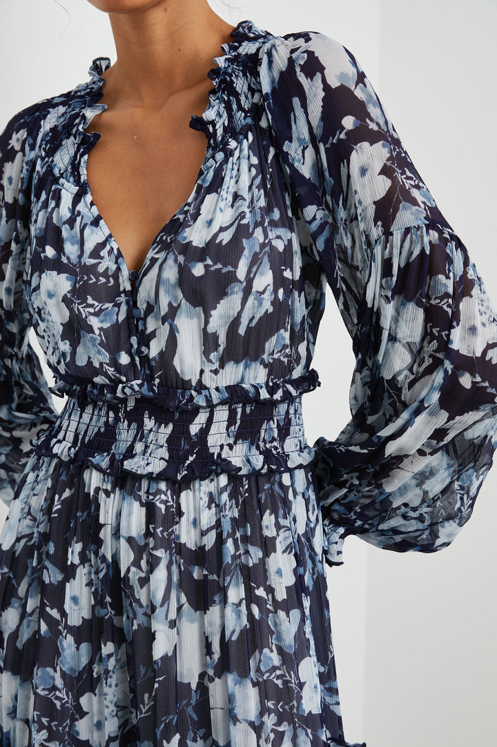 Frederica Long-Sleeve Maxi Dress with a V Neck, a Shirred Collar and Waist, Elastic Cuffs, and a Tiered Skirt in Indigo Blossoms Colorway, with blossoms in Blues on Indigo - Front View Featured on Model