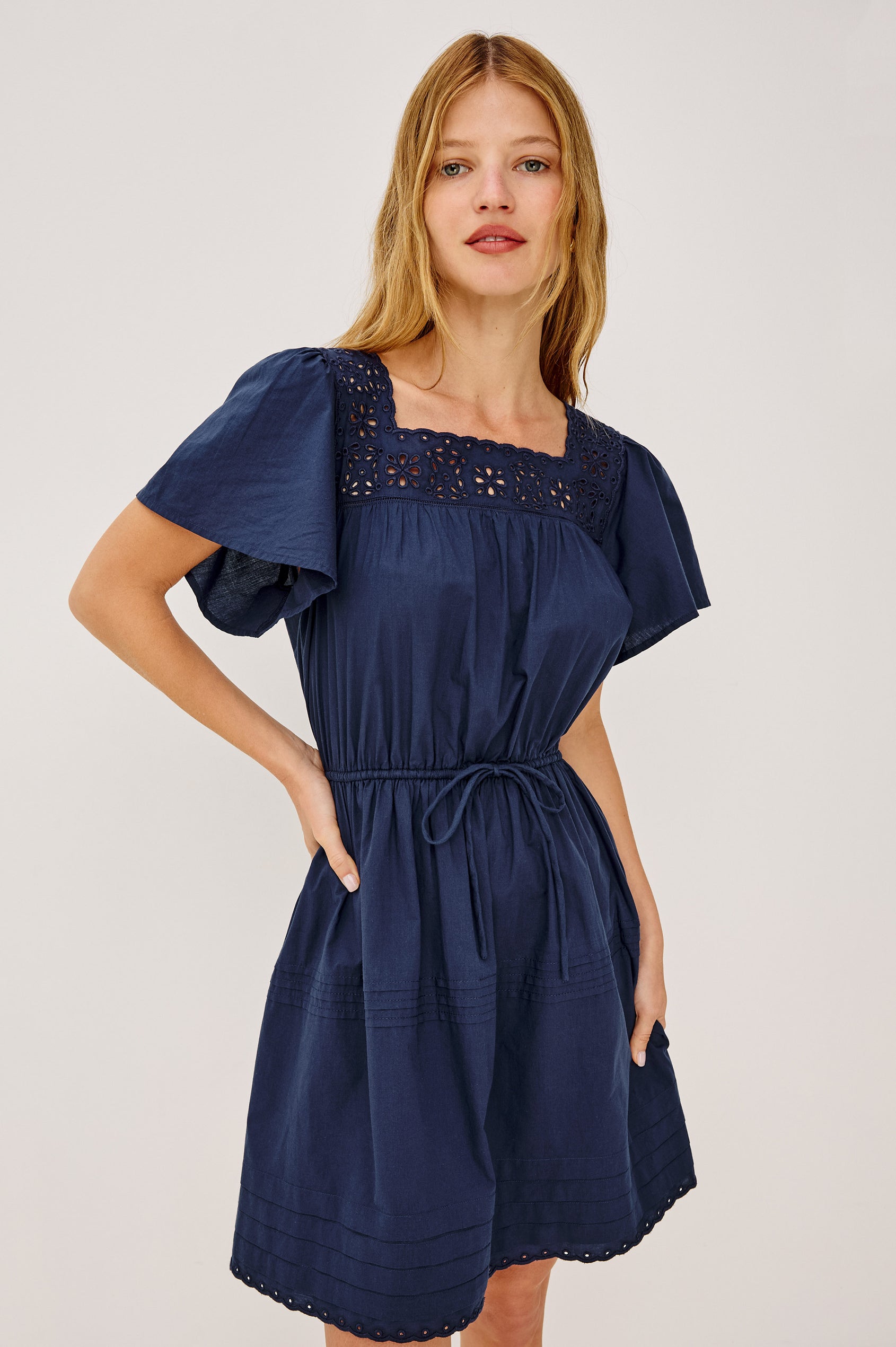 Gale Mini Dress in Cotton Voile With Embroidered Square Neckline, Drawstring Waist Ties, Short Flutter Sleeves, Pintuck Detailing, and Lined Skirt in Navy Colorway - Upper Body Front View Featured on Model