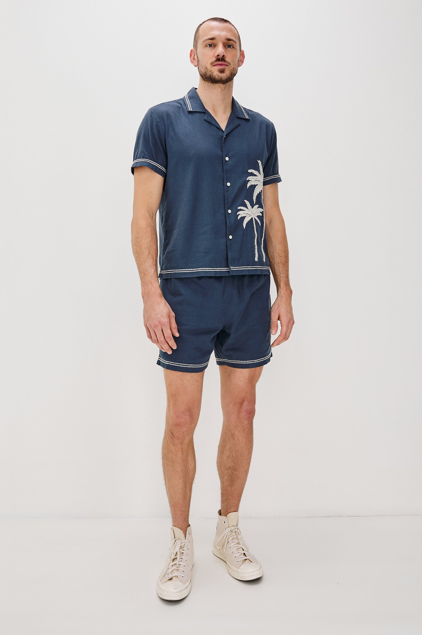 Gibson Button Front Shirt with Open Relaxed Collar, Short Sleeves, White Contrast Buttons, Contrast White Stitching at Collar and Hems and Embroidered White Palm Trees on Left Side in Navy White Palm Colorway. Full Body Front View Shown on Model.