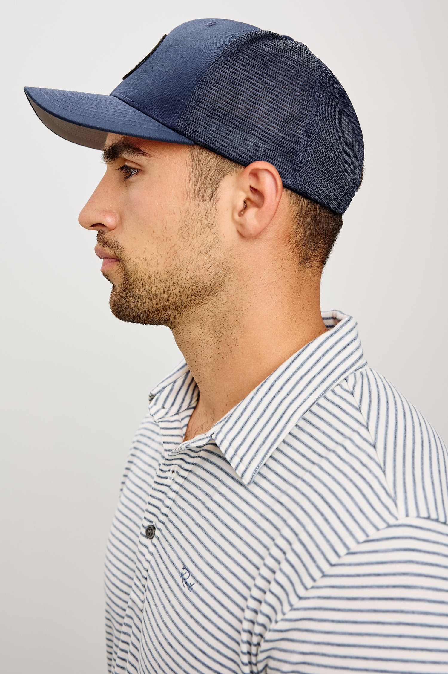 Golf Hat With Embroidered Branded Patch at Front, Adjustable Snapback, Mesh Back, and 6-Panel Construction in Navy Colorway - Upper Body Side View Featured on Model