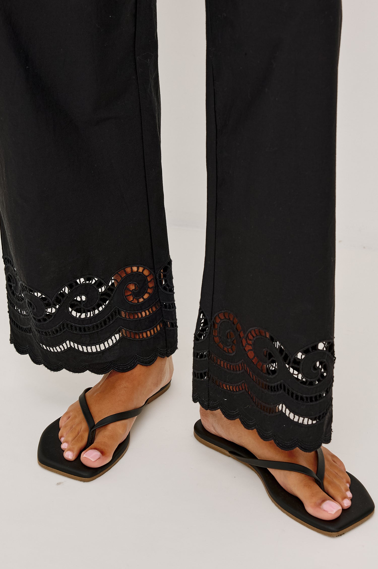 Henrik High-Rise High-Waisted Pant With Wide Smocked Waistband, Side Pockets, Straight Legs, and Scalloped Ladder Embroidered Hem in Black Colorway - Lower Body Close Up View Featured on Model