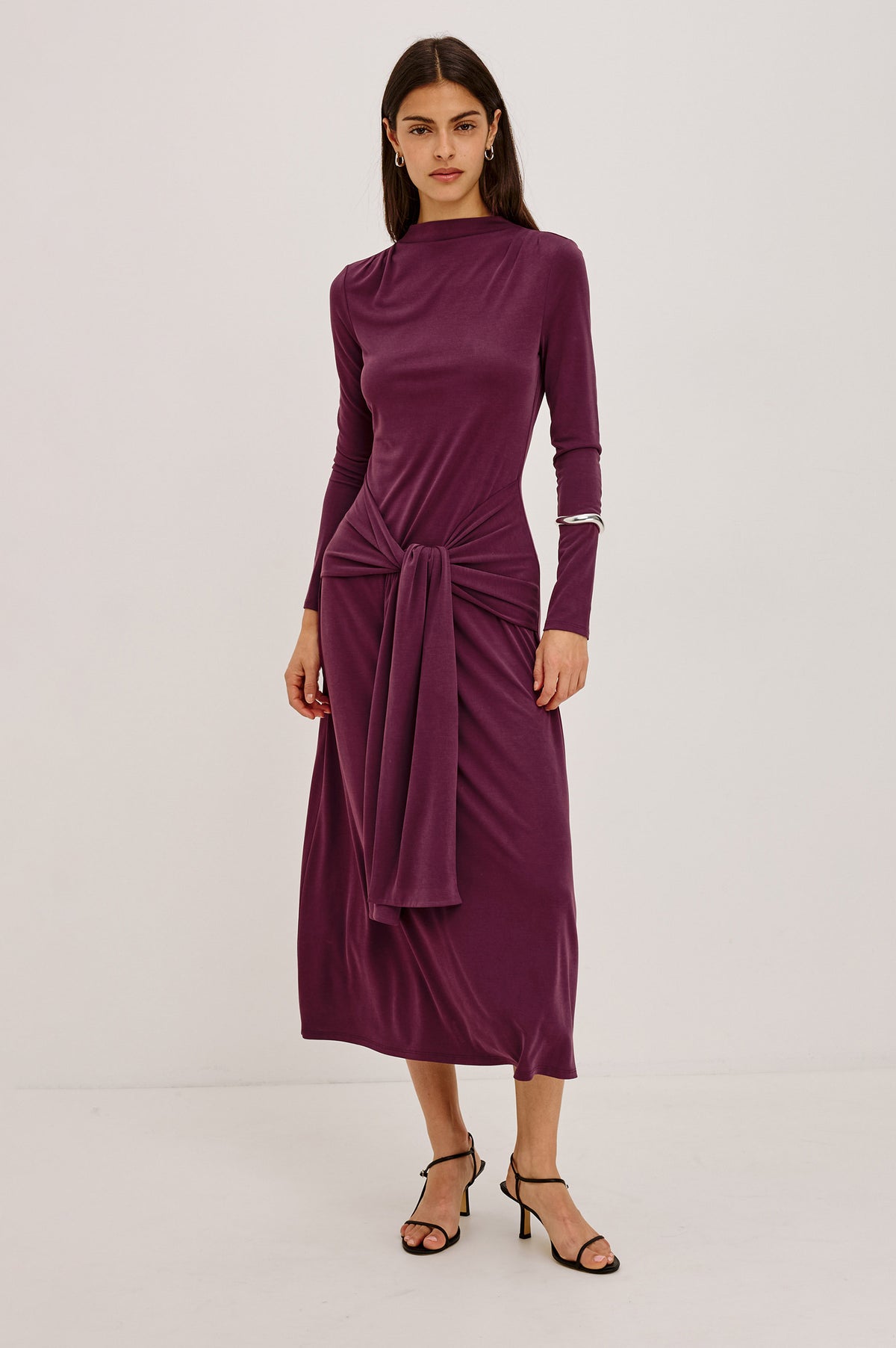 Hollis Midi Dress in Soft Jersey With Mockneck, Front Waist Ties, Pleated Shoulders, Long Sleeves, and A-Line Skirt in Wine Colorway - Full Body Front View Featured on Model.
