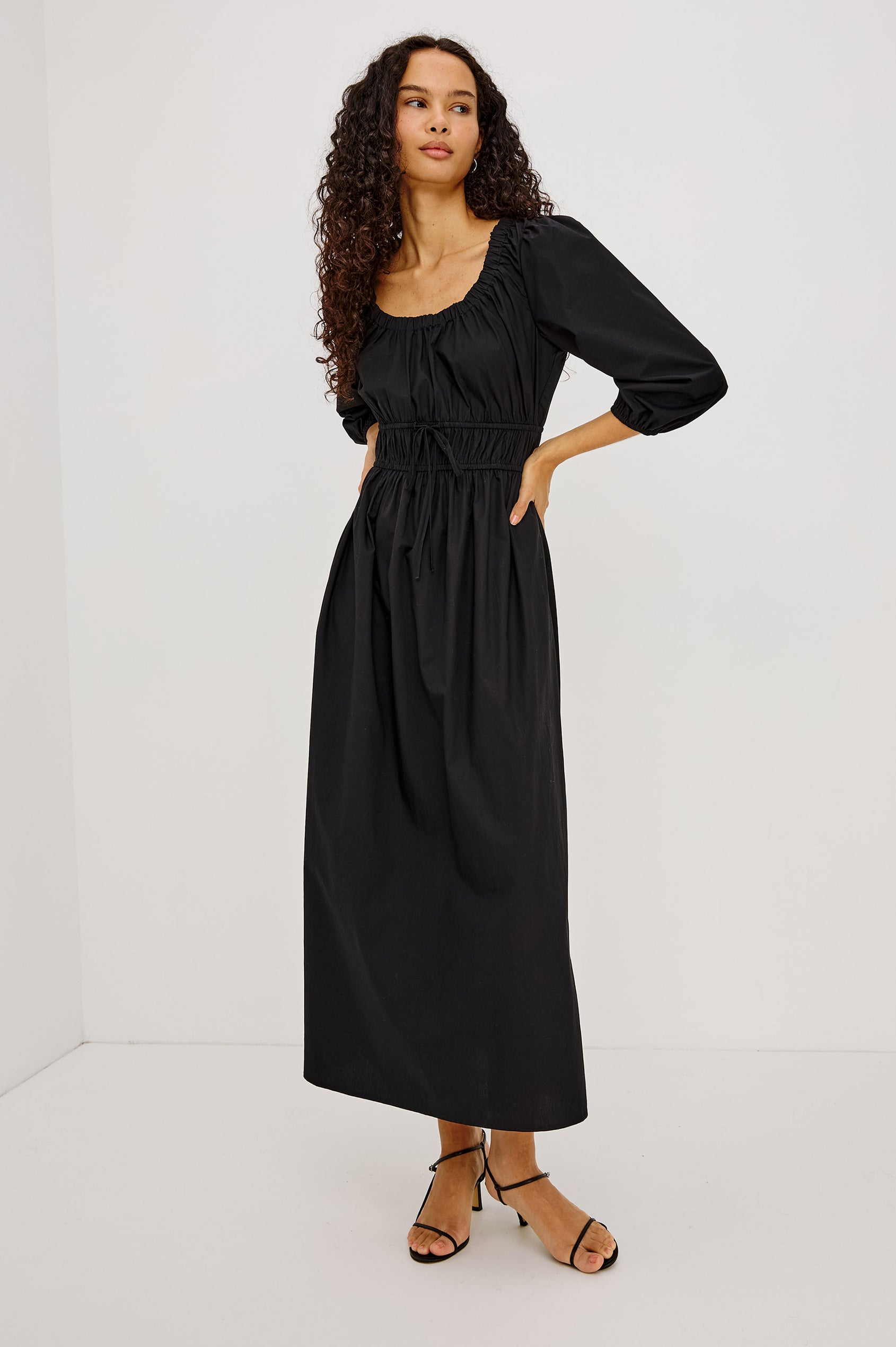 Isabelle Maxi Dress in Cotton Poplin With Ruched Scoop Neck, Puff Elbow-Length Sleeves, and Laddered Shirred Waist With Ties in Black Colorway - Full Body Front View Featured on Model