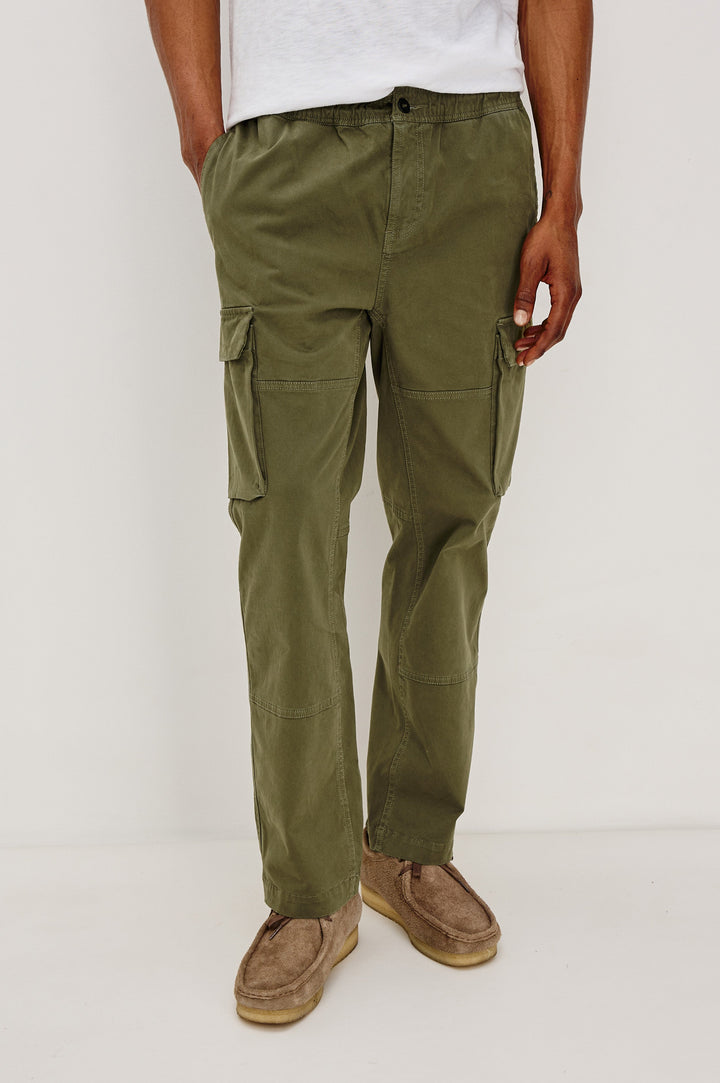 Jaiden Pants with an Elastic, Button Waist with Zip Fly, Two Front Pockets, Two Side Flap Pockets, and Two Back Flap Pockets in True Olive Colorway - Front View Featured on Model