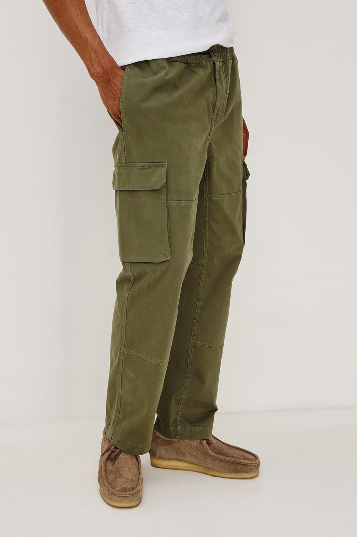 Jaiden Pants with an Elastic, Button Waist with Zip Fly, Two Front Pockets, Two Side Flap Pockets, and Two Back Flap Pockets in True Olive Colorway - Front View Featured on Model