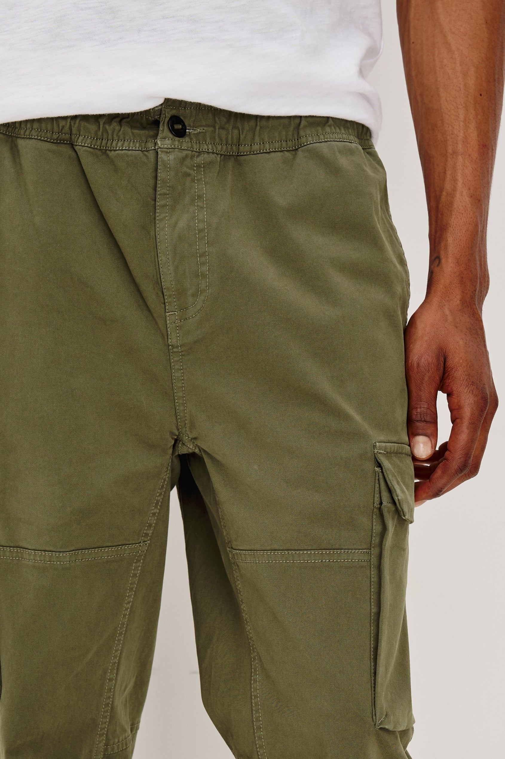 Jaiden Pants with an Elastic, Button Waist with Zip Fly, Two Front Pockets, Two Side Flap Pockets, and Two Back Flap Pockets in True Olive Colorway - Front Detail View Featured on Model