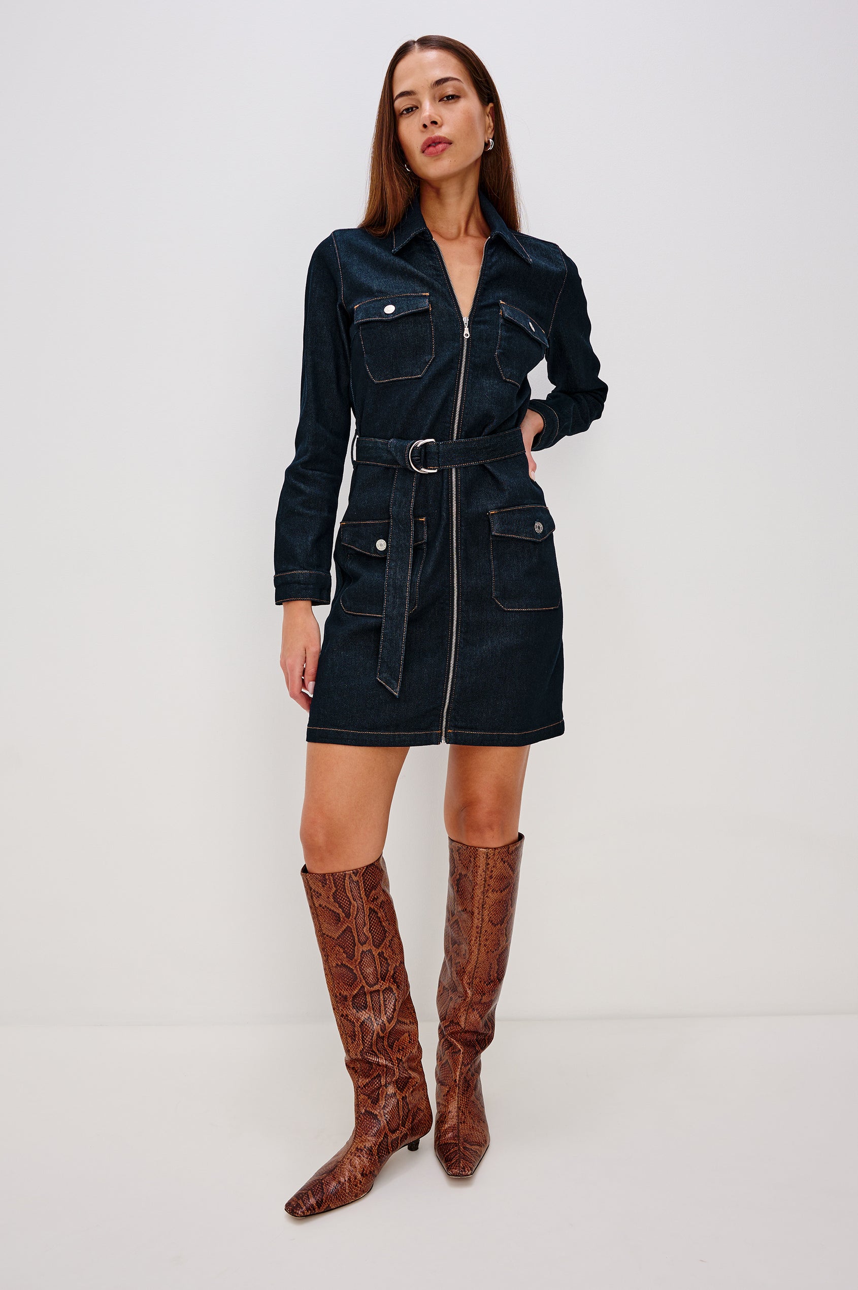 Jefferson is a long sleeve mini denim dress, featuring utility-inspired details and an o-ring adjustable waist belt in Midnight Blue colorway, a rinse wash. Front full body view featured on model.