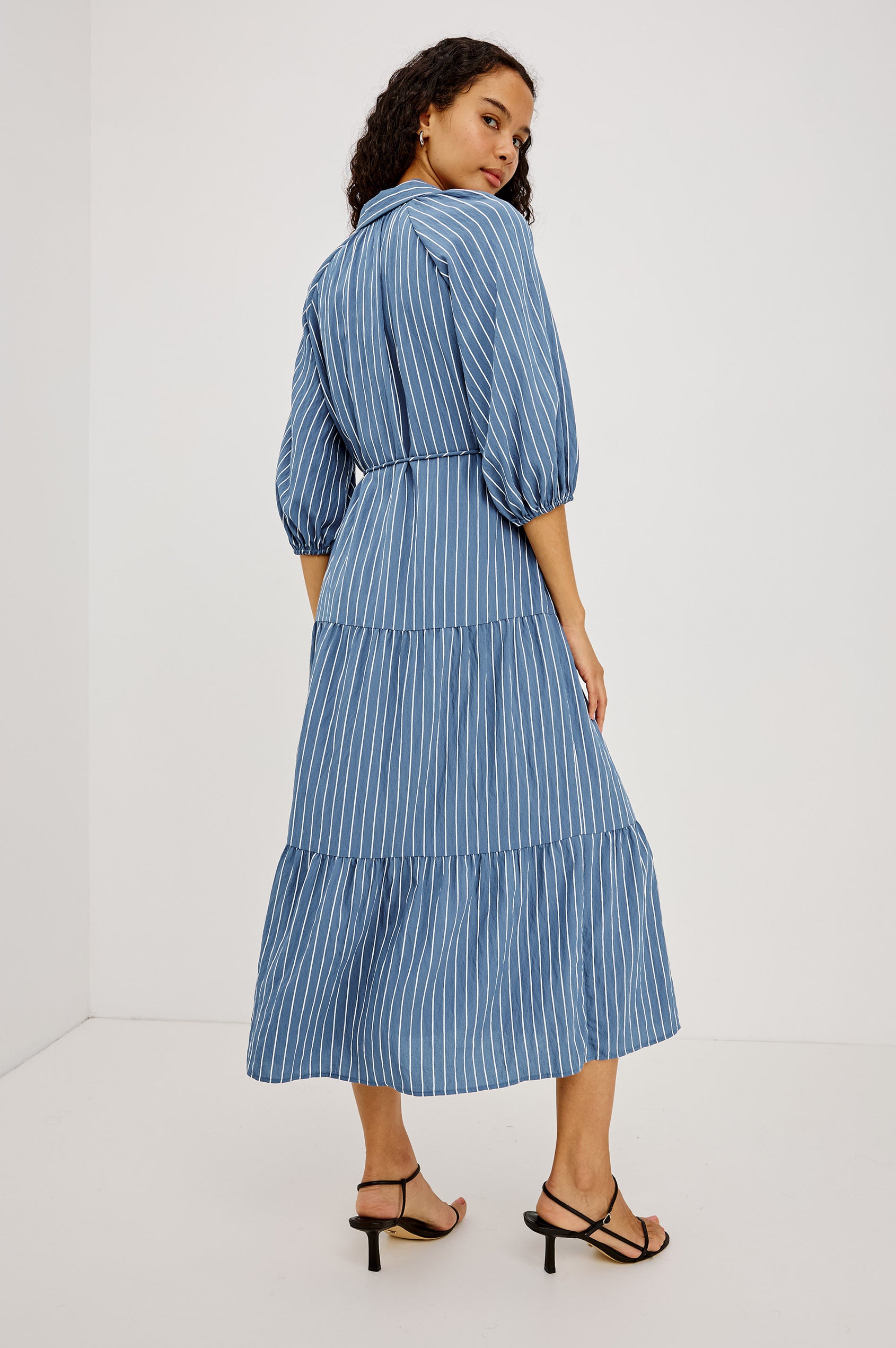 June Maxi Dress in Soft Crinkle Shirting With Three-Quarter Puff Sleeves, Point Collar, Full Front Button Placket, and Self-Tie Waist in Washed Indigo Stripe Colorway - Full Body Back View Featured on Model