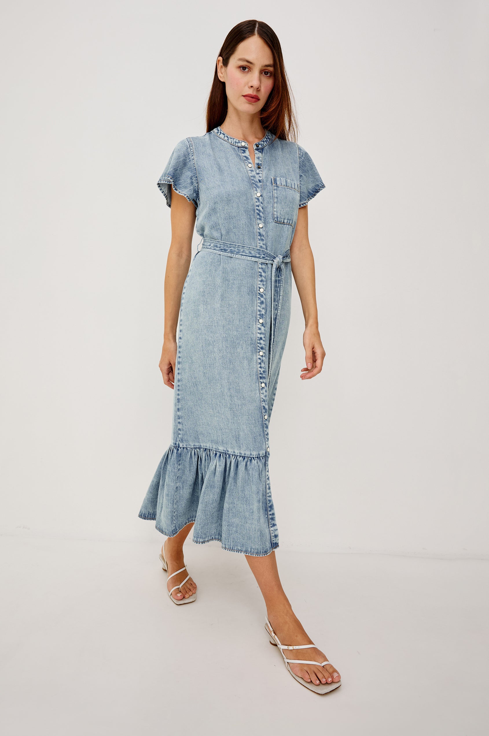 Kahlo TENCELâ„¢ Denim Shirt Dress With Short Flutter Sleeves Front Buttons a Single Chest Patch Pocket Adjustable Belted Ties Ruffle Hem in Faded Indigo Colorway - Full Body Front View Featured on Model
