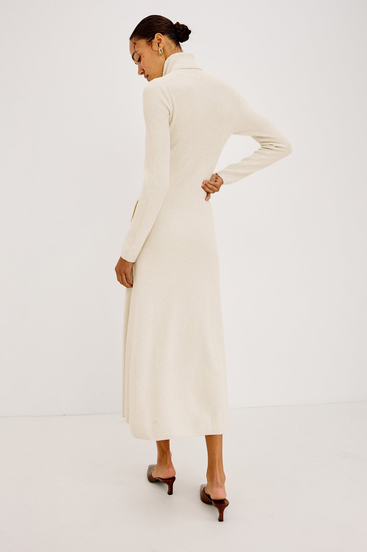 Kat Maxi Dress in Ribbed Cotton Blend With Foldover Turtleneck Button Neckline, Long Sleeves, Fitted Silhouette, Long Sleeves, Side Placket, and Subtle Flare at Hem in Ivory Colorway - Full Body Back View Featured on Model
