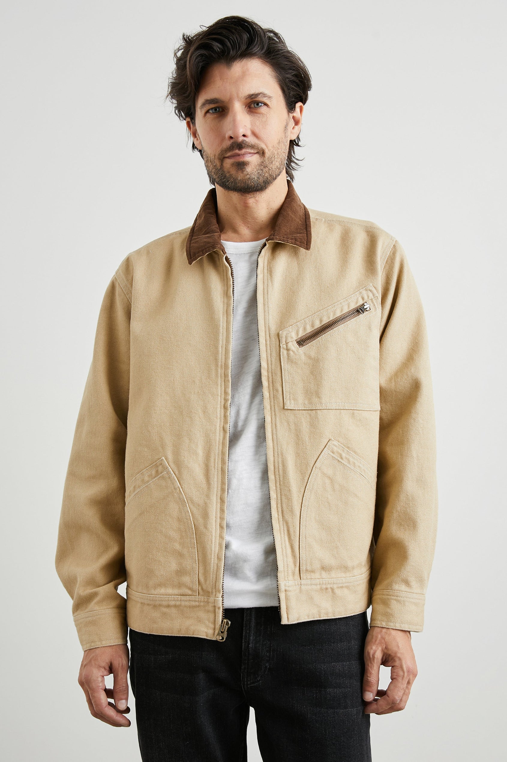 Ketter Zip Up Jacket with Two Curved Front Patch Pockets, a Diagonally Zippered Chest Patch Pocket and Adjustable Button Straps on the Hem in Duck Colorway, a Tan with a Darker Brown Collar - Front View Featured on Model