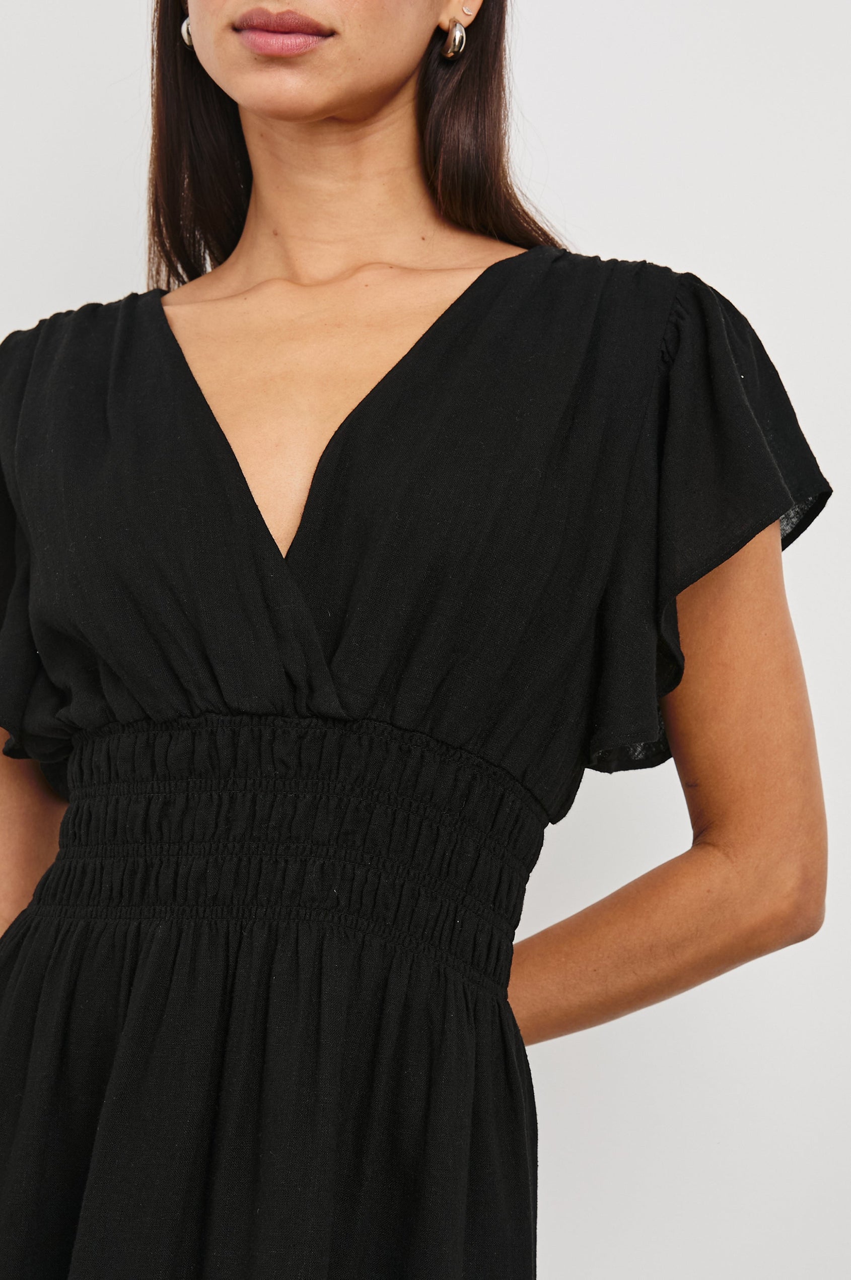 Kimora Above-Knee Dress with Flutter Sleeves, a V Neckline, a Cinched Waist and a Tiered Skirt in Black Colorway - Front View Featured on Model
