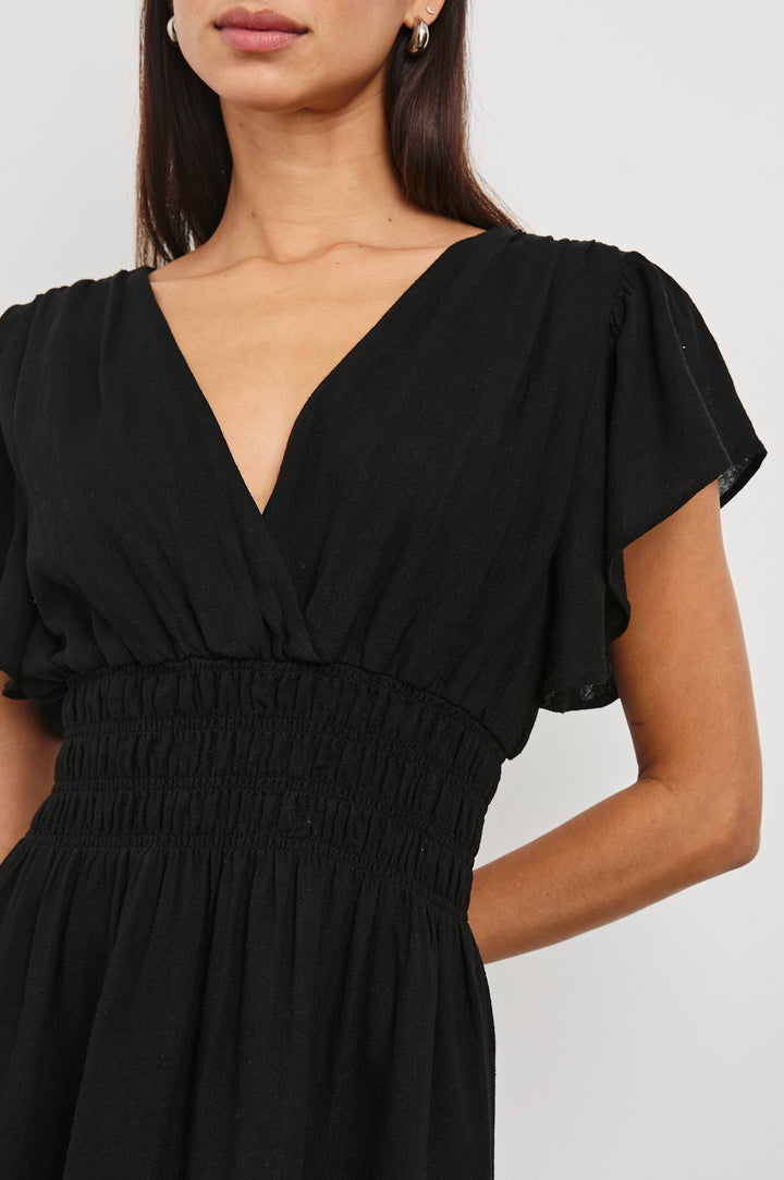 Kimora Above-Knee Dress with Flutter Sleeves, a V Neckline, a Cinched Waist and a Tiered Skirt in Black Colorway - Front View Featured on Model