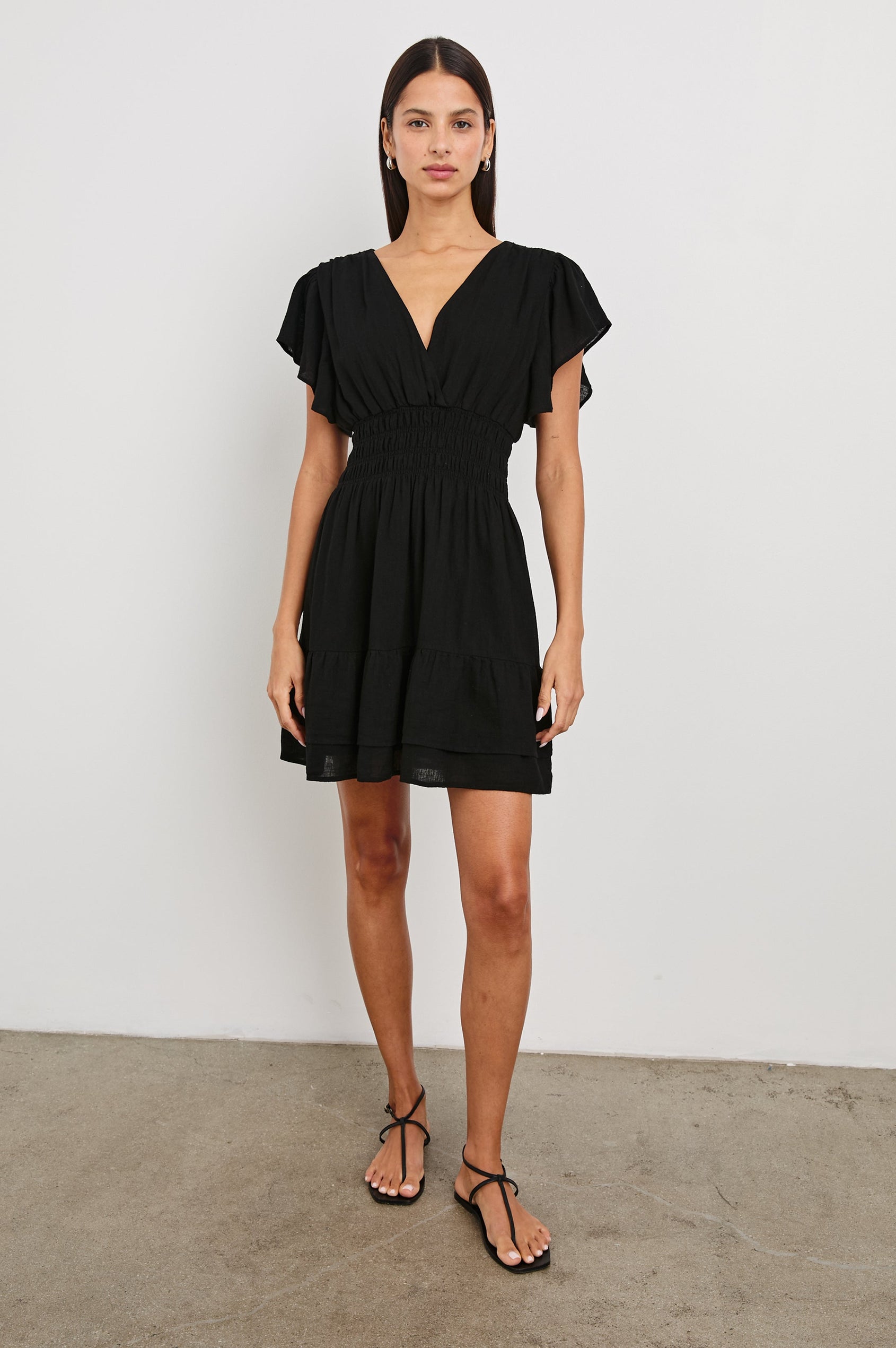 Kimora Above-Knee Dress with Flutter Sleeves, a V Neckline, a Cinched Waist and a Tiered Skirt in Black Colorway - Front Full Body View Featured on Model
