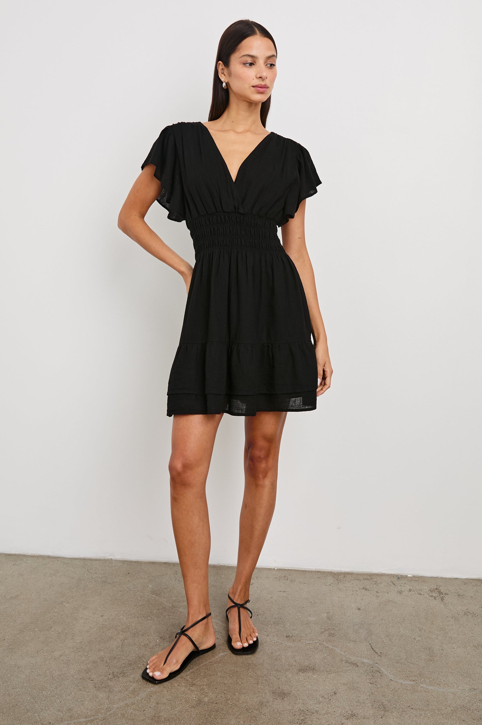 Kimora Above-Knee Dress with Flutter Sleeves, a V Neckline, a Cinched Waist and a Tiered Skirt in Black Colorway - Front Full Body View Featured on Model