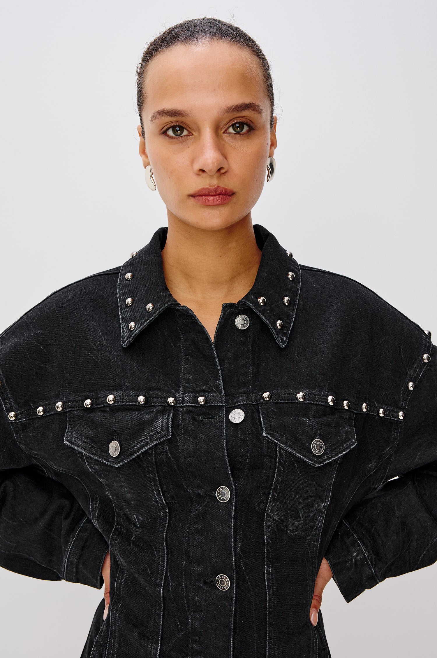 Ladera Mini Dress in Denim With Subtle Stretch, Drop Shoulders, Collar, Relaxed Long Balloon Sleeves, Nail-Back Studs, Front Buttons, A-Line Shape, and Adjustable Back Strap in Black Stone Studded Colorway - Upper Body Close Up Front View Featured on Model