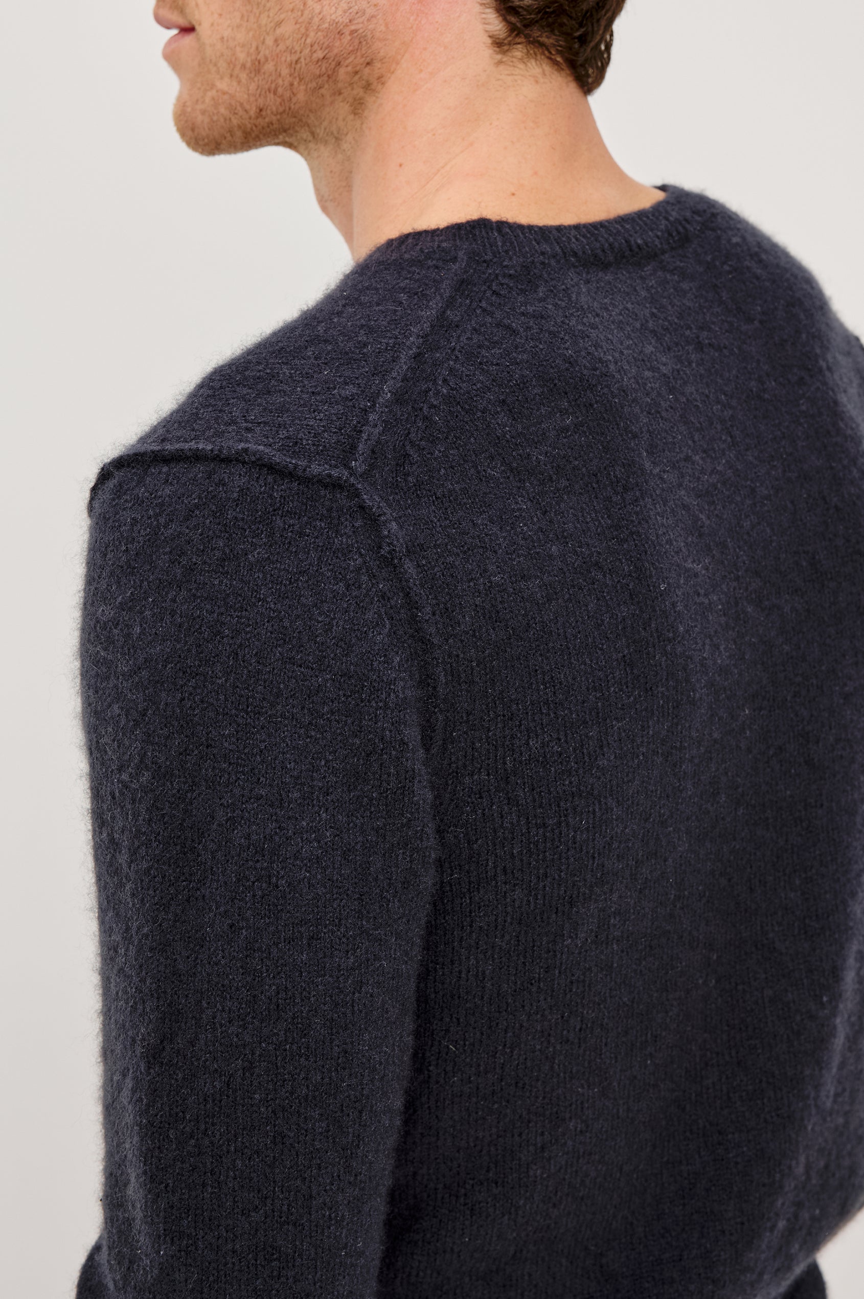The Laurent is a relaxed-fit sweater with dropped shoulders, long sleeves, and linking-stitch detailing at the shoulders in Midnight colorway. Back detail view featured on model.