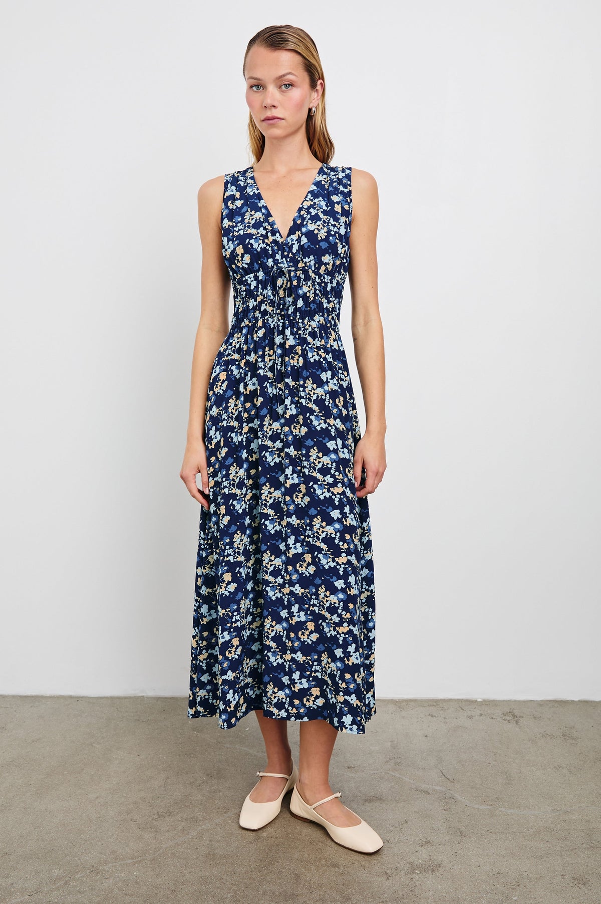Lilith Sleeveless Midi Dress with Wide Shoulder Straps, a Deep V neck, a Cinched Waist with Drawstring, and a Back Neck Tie in Navy Flora Colorway, with flowers in creams and blues on Navy - Front Full Body View Featured on Model  
