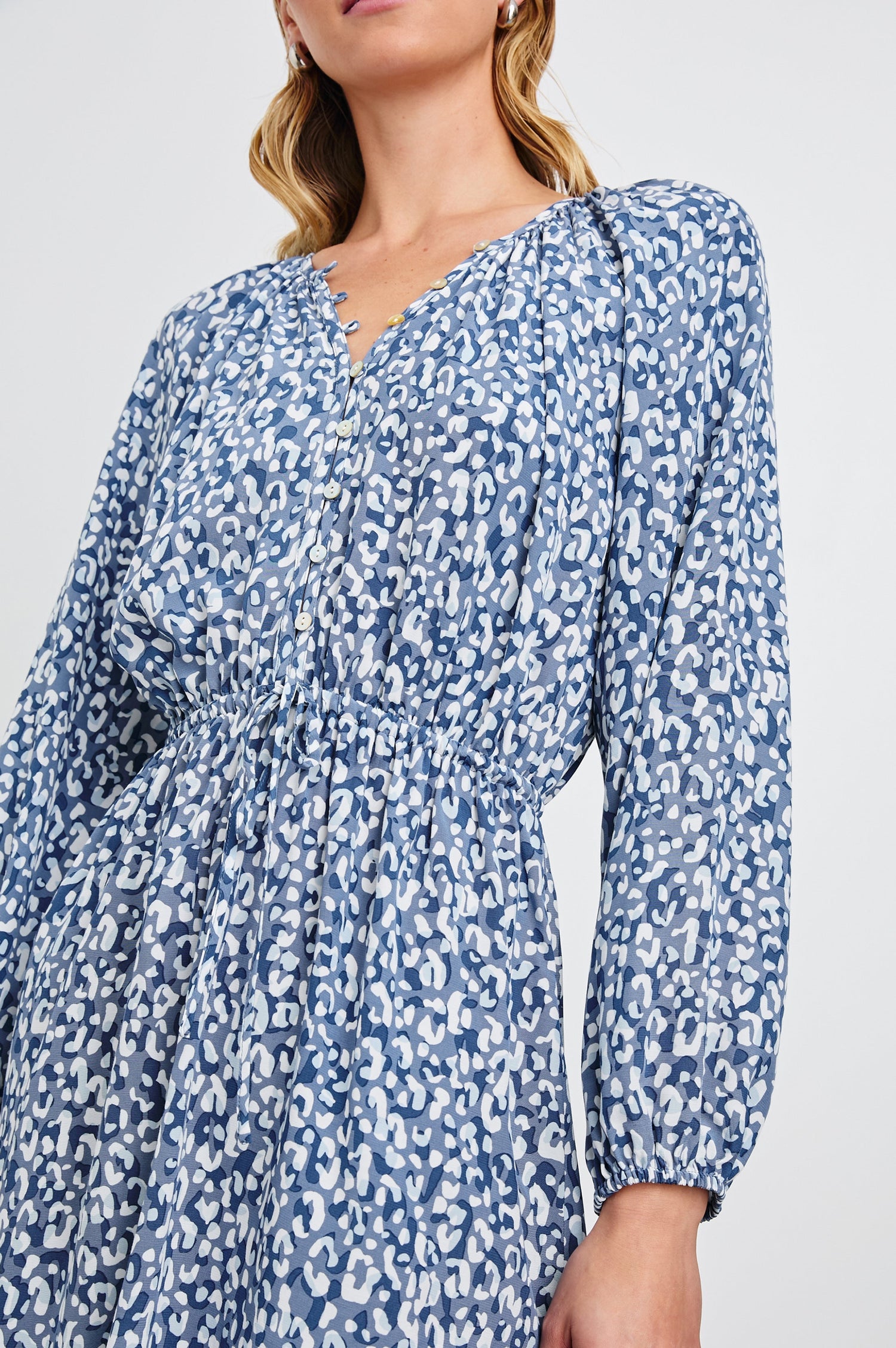 Linnea Mid-Thigh, Long-Sleeve Dress with a V Neck, Buttons down the Bodice, a Smocked Waist with Drawstring, and Elastic Cuffs in Blue Mixed Cheetah Colorway, Spots in Blues and White - Front View Featured on Model
