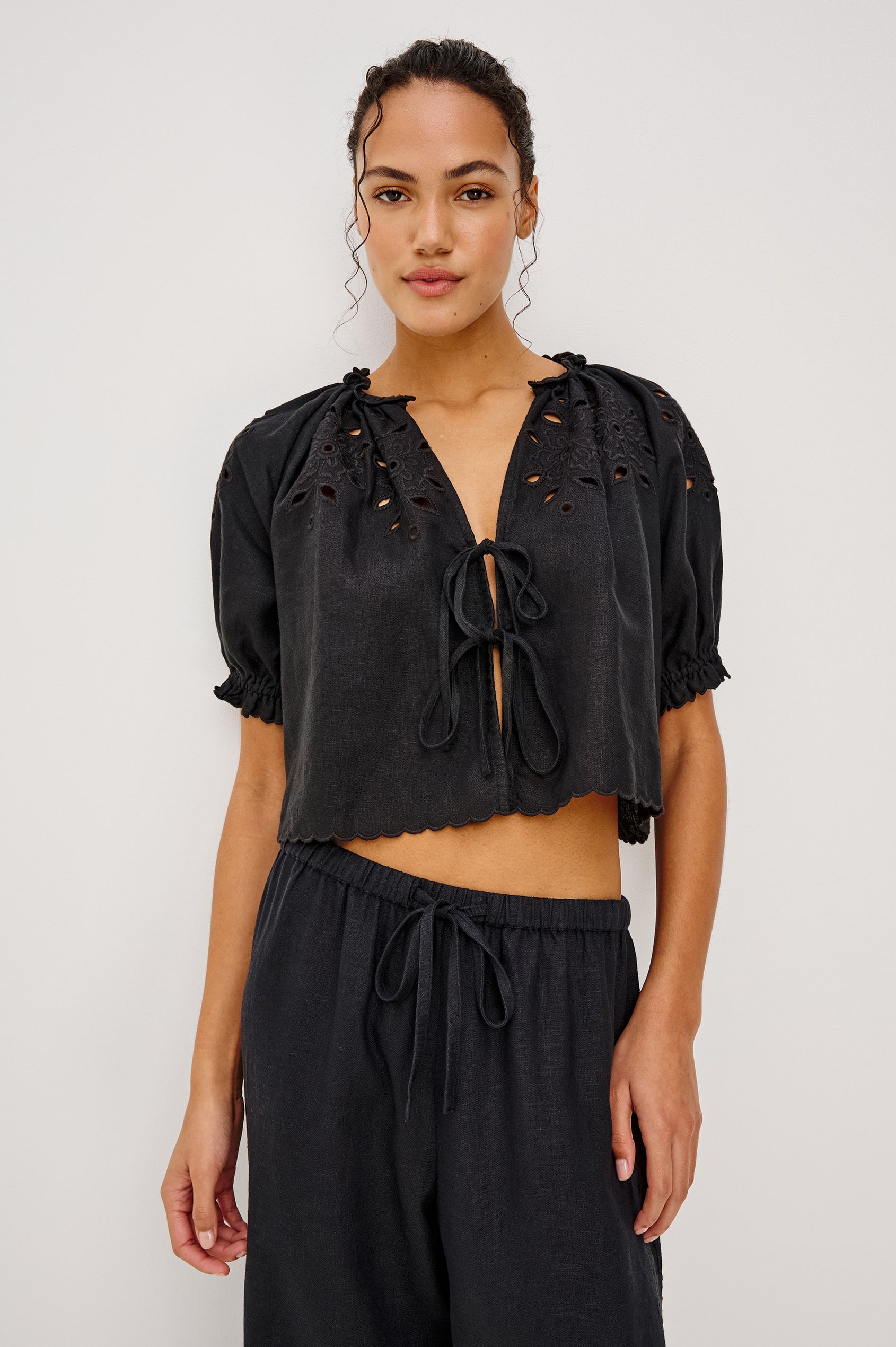 Lizbeth Milkmaid Top in Linen With Floral Eyelet Cutwork Plunging Tie-Front V-Neckline Front Ties Relaxed FIt Short Puff Sleeves in Black Ctolorway - Upper Body Front View Featured on Model