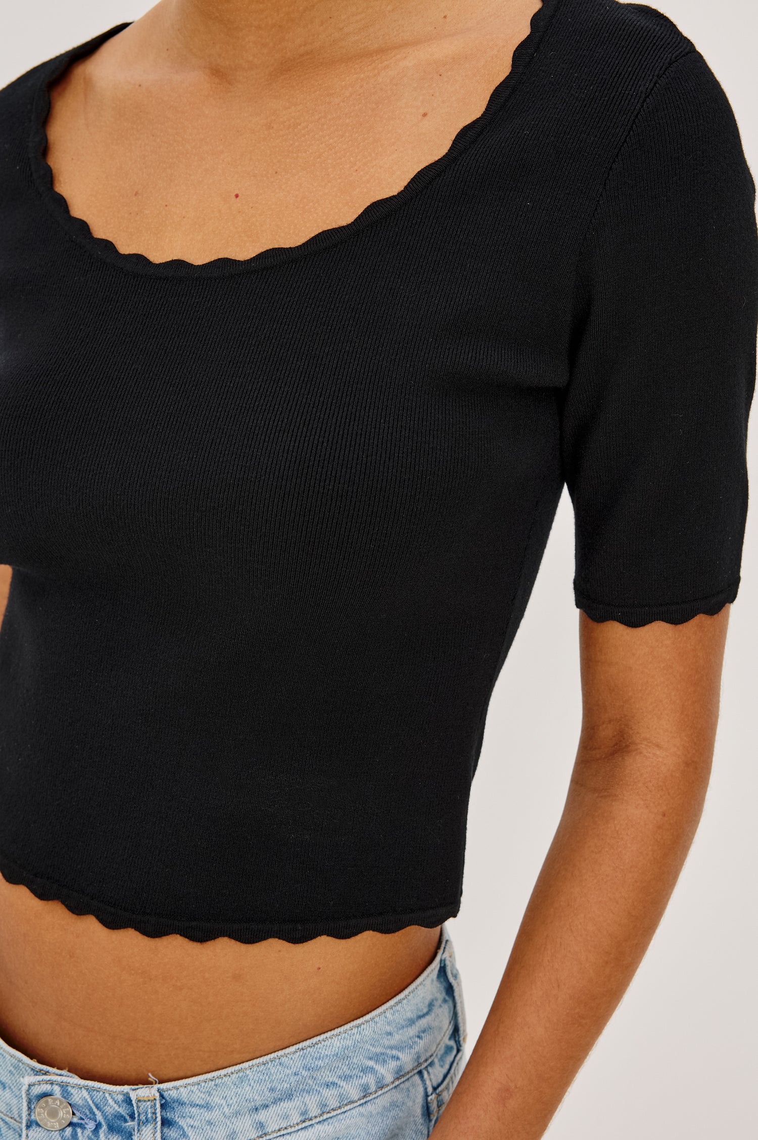 Louanna Fitted Cropped Top in Compact Knit With Scallop-Trimmed Scoop Neckline, Short Sleeves, and Hem in Black Colorway - Upper Body Close Up Front View Featured on Model
