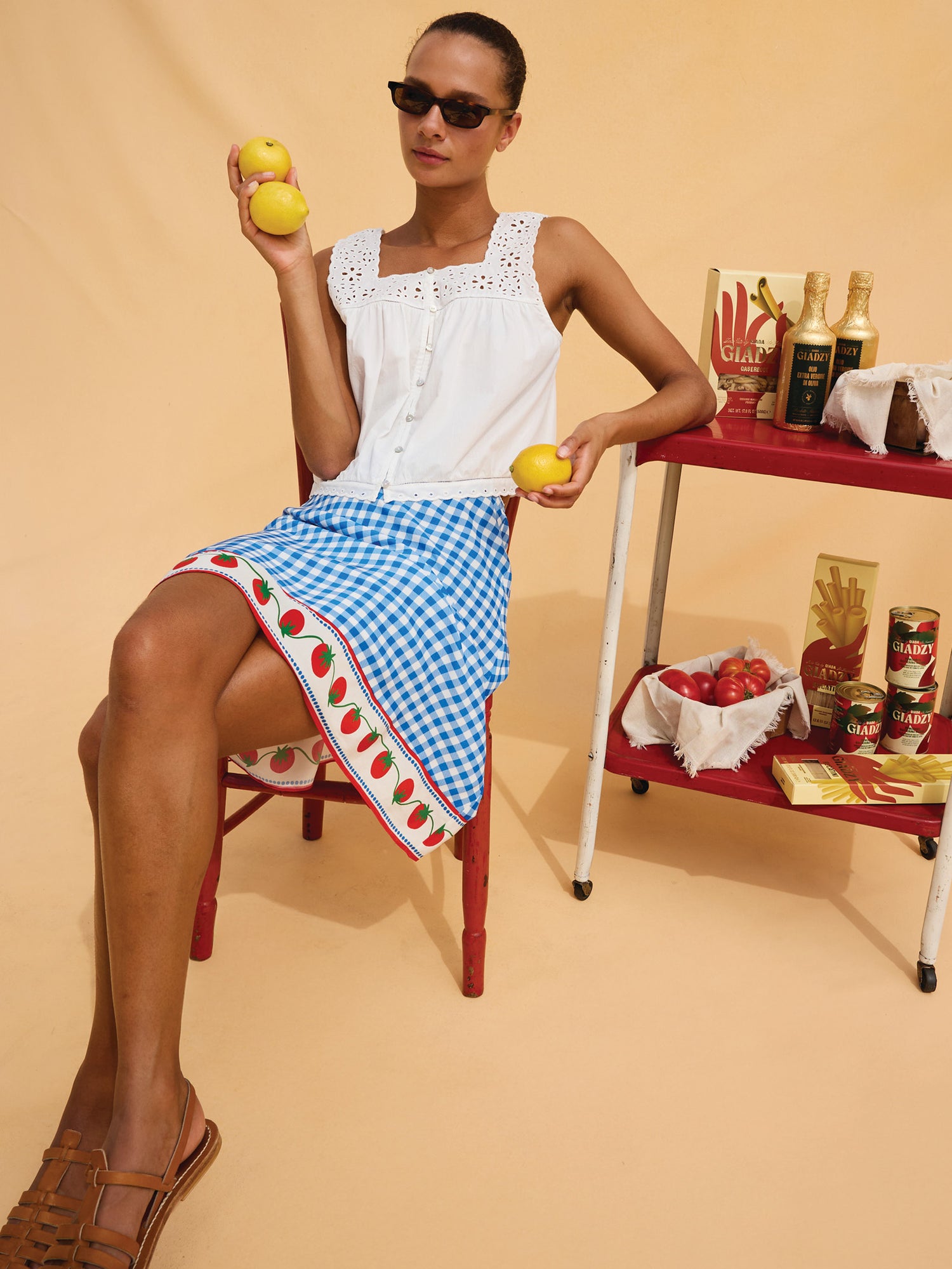 Woman holding lemons in a kitchen setting with a table and various items.