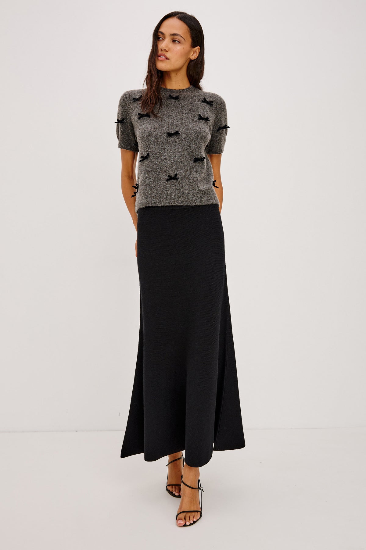 Michele Sweater in Wool Blend With an Off-The-Shoulder Neckline and Bow Applique in Charcoal Colorway - Full Body Front View Featured on Model.