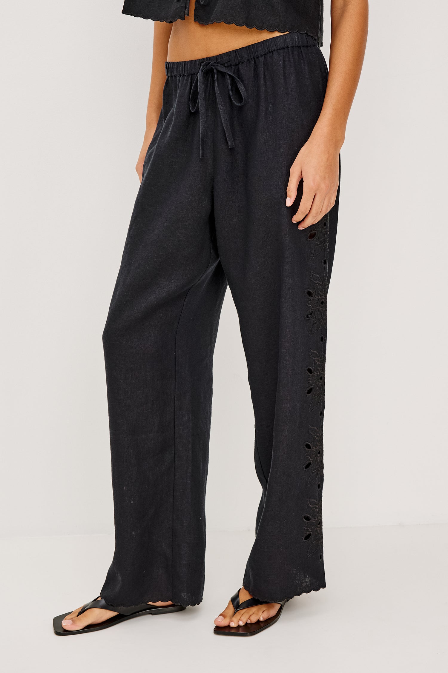 Made from midweight linen the Mirina Pant has an elastic waistband with adjustable center front ties side pockets loose straight legs and intricate floral cutwork and scalloped trim.