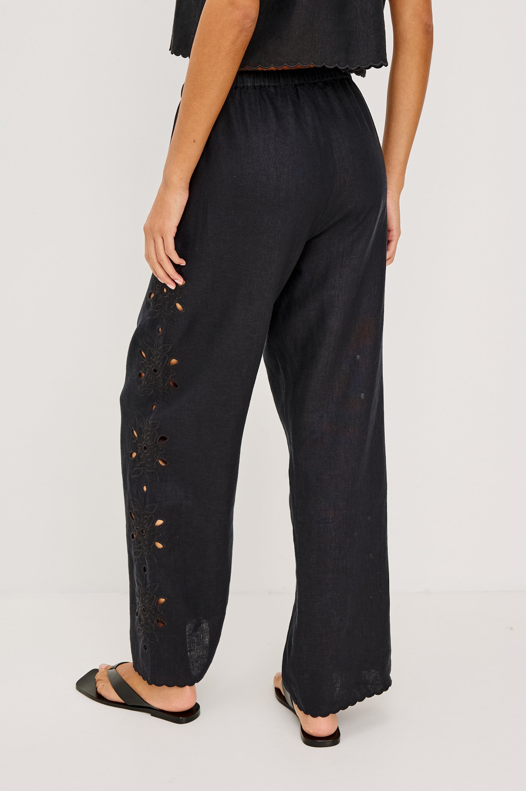 Made from midweight linen the Mirina Pant has an elastic waistband with adjustable center front ties side pockets loose straight legs and intricate floral cutwork and scalloped trim.