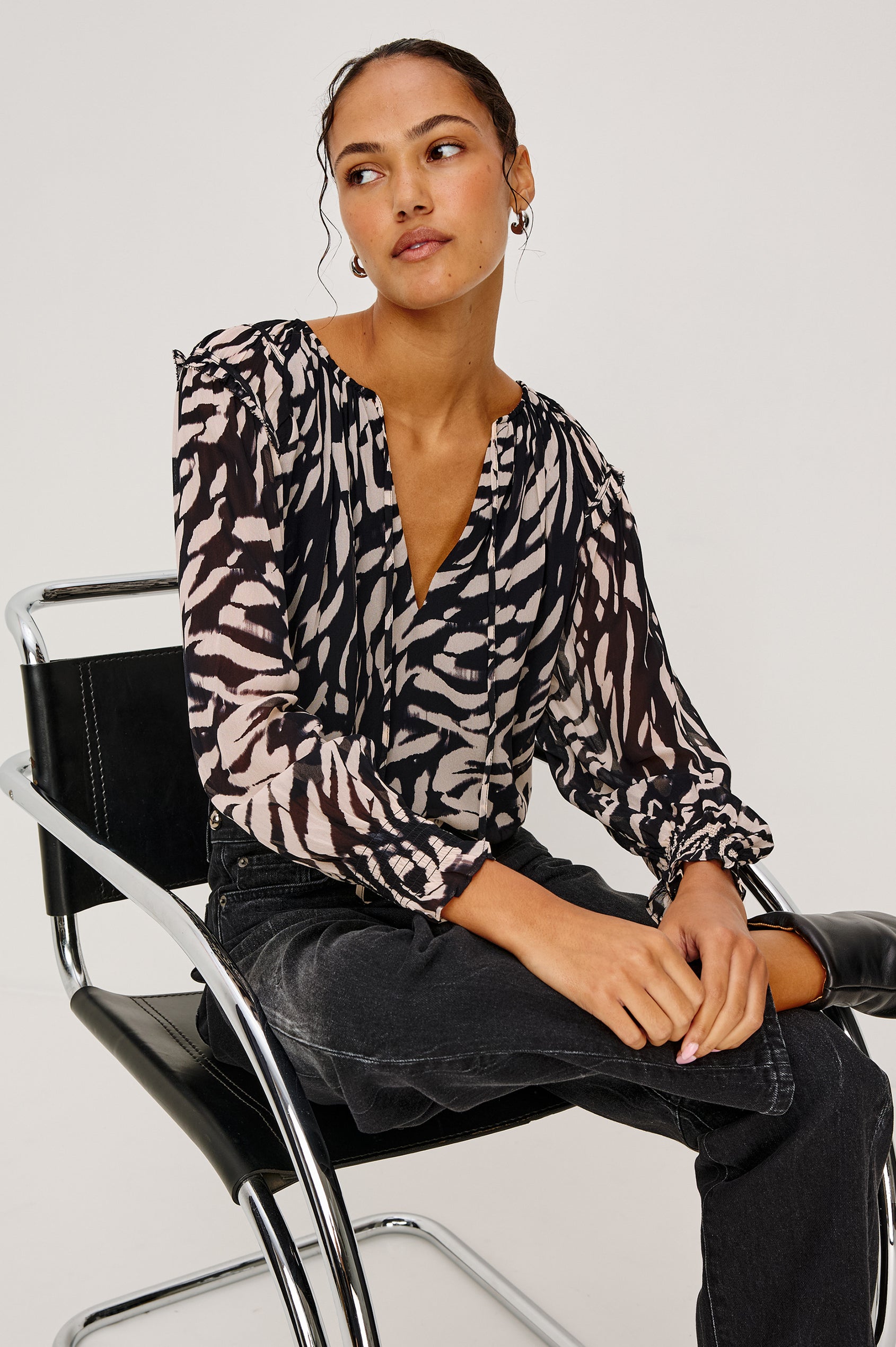 Mirna Blouse in Chiffon With Self-Tie V-Neckline, Loose Boxy Fit, Ruffle Trim, Balloon Sleeves with Smocked Cuffs in Ivory Tiger Stripe Colorway - Upper Body Front View Featured on Model Sitting