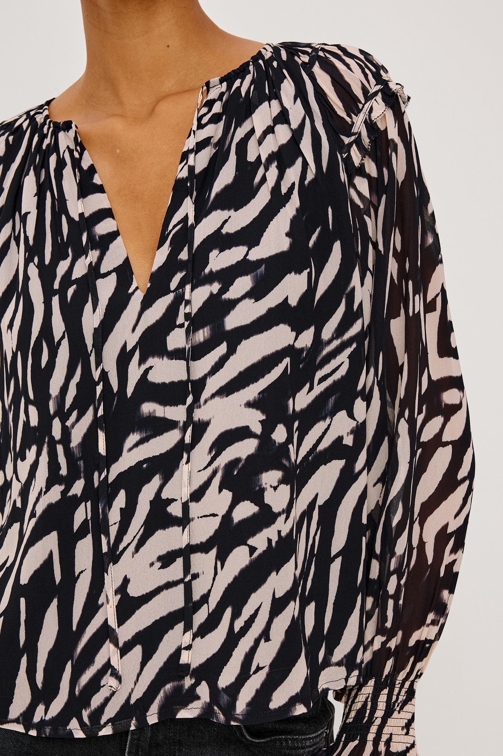 Mirna Blouse in Chiffon With Self-Tie V-Neckline, Loose Boxy Fit, Ruffle Trim, Balloon Sleeves with Smocked Cuffs in Ivory Tiger Stripe Colorway - Close Up Upper Body Front View Featured on Model Sitting