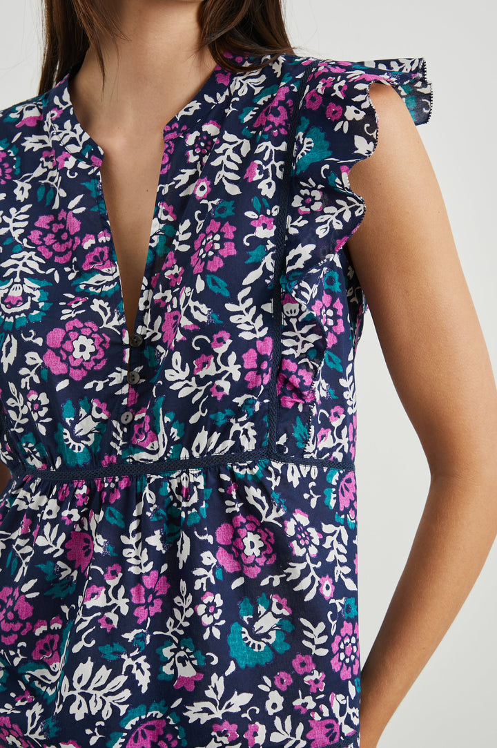 Misha Short Sleeve Top with Flutter Sleeves, a Deep V Neck, and Vertical and Horizontal Black Seams in Woodblock Floral Colorway, Pink, White and Green on Navy - Front View Featured on Model 