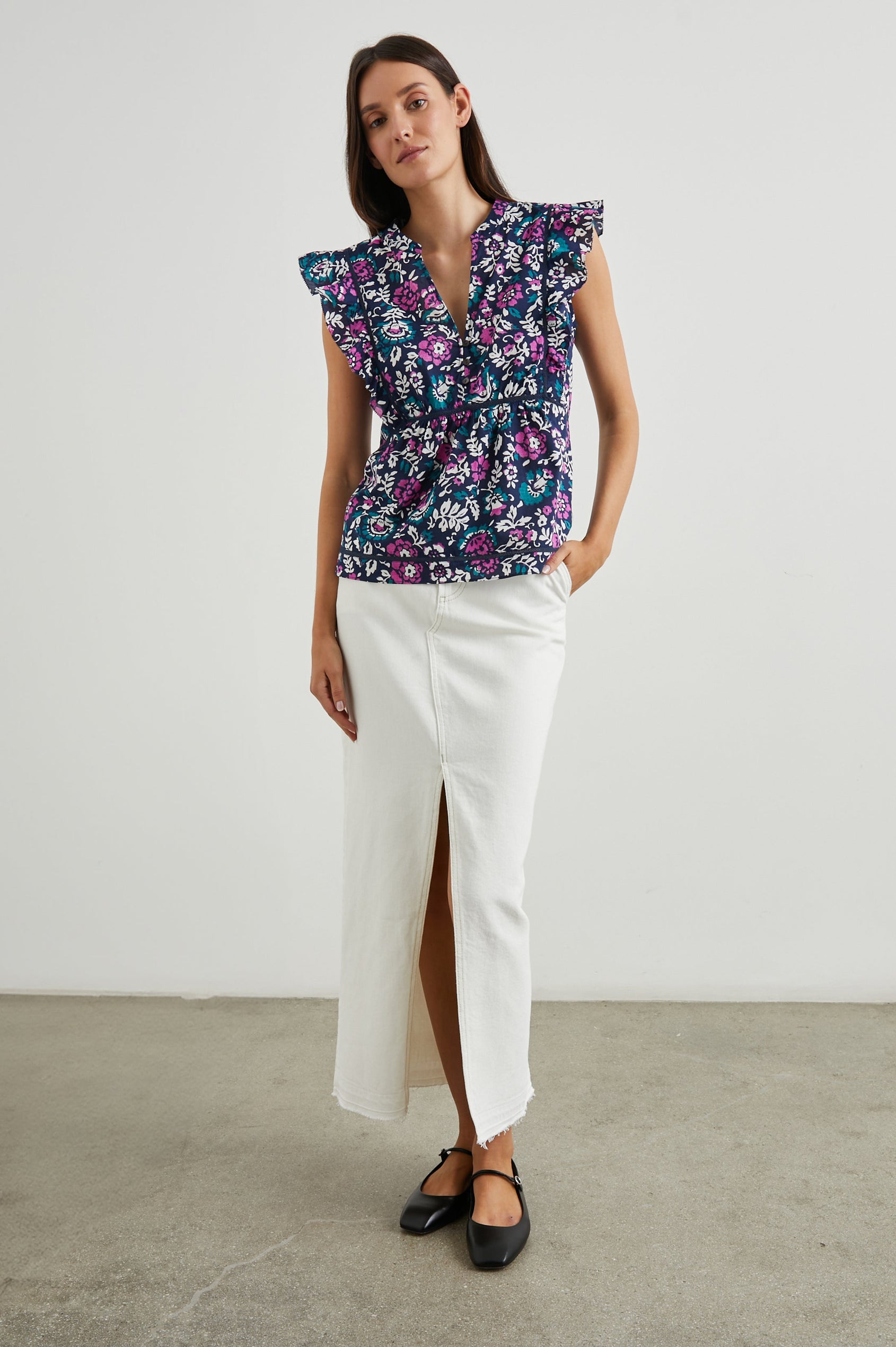 Misha Short Sleeve Top with Flutter Sleeves, a Deep V Neck, and Vertical and Horizontal Black Seams in Woodblock Floral Colorway, Pink, White and Green on Navy - Front Full Body View Featured on Model 