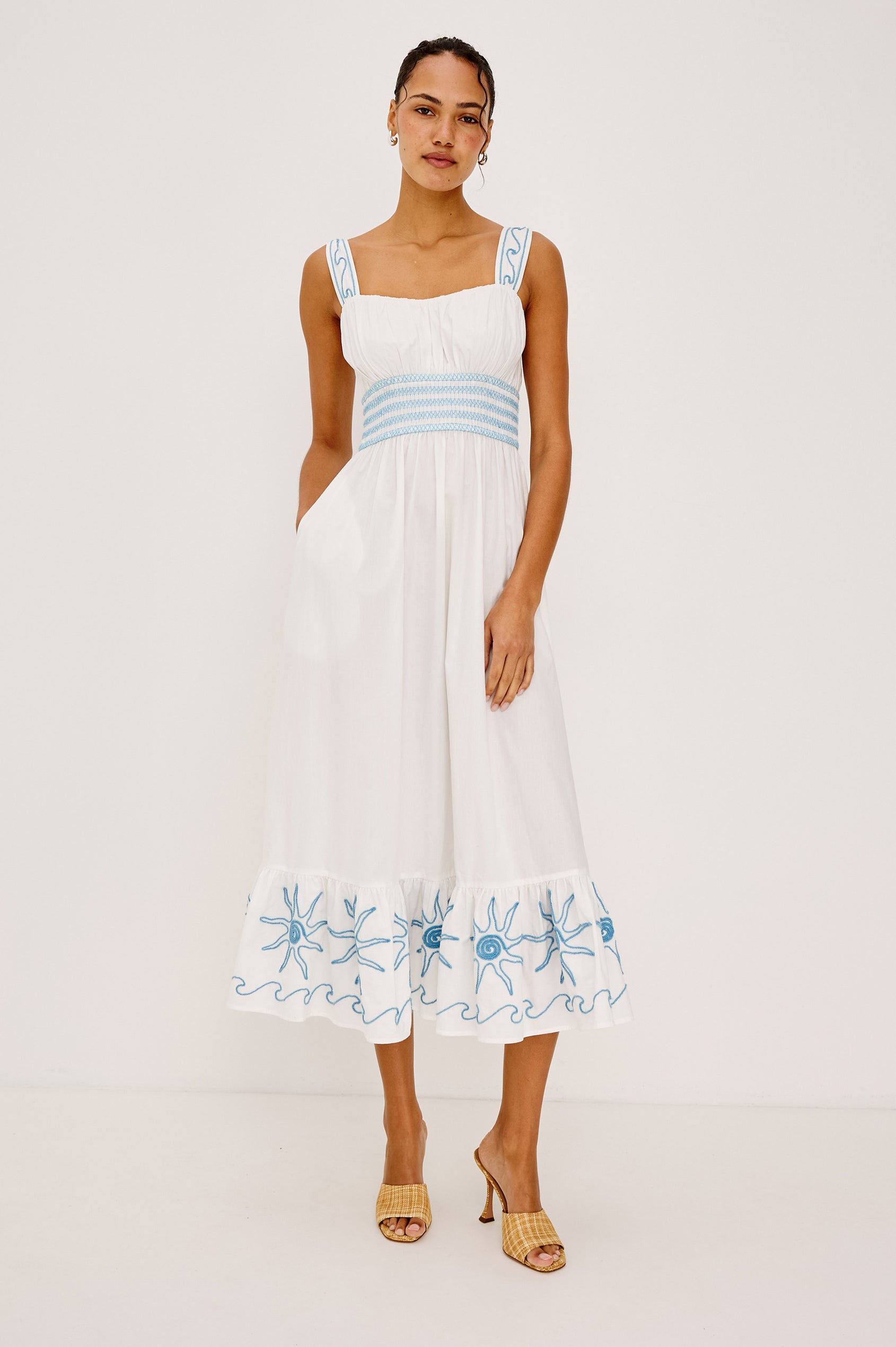 Moira Midi Dress in Cotton Poplin With Wide Embroidered Shoulder Straps Soft Sweetheart Neckline Smocked Empire Waist Fully Lined Skirt With Floral Cutwork at Hem in a White Colorway With Blue Embroidery Details - Full Body Front View Featured on Model