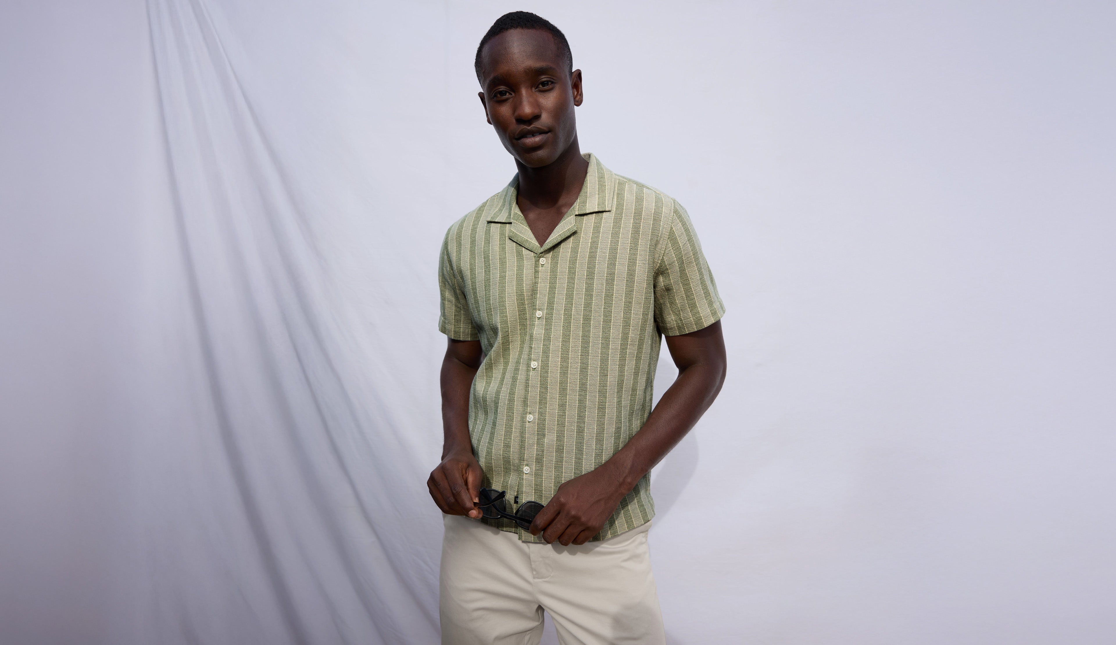 Man wearing a green striped shirt and beige pants against a white background