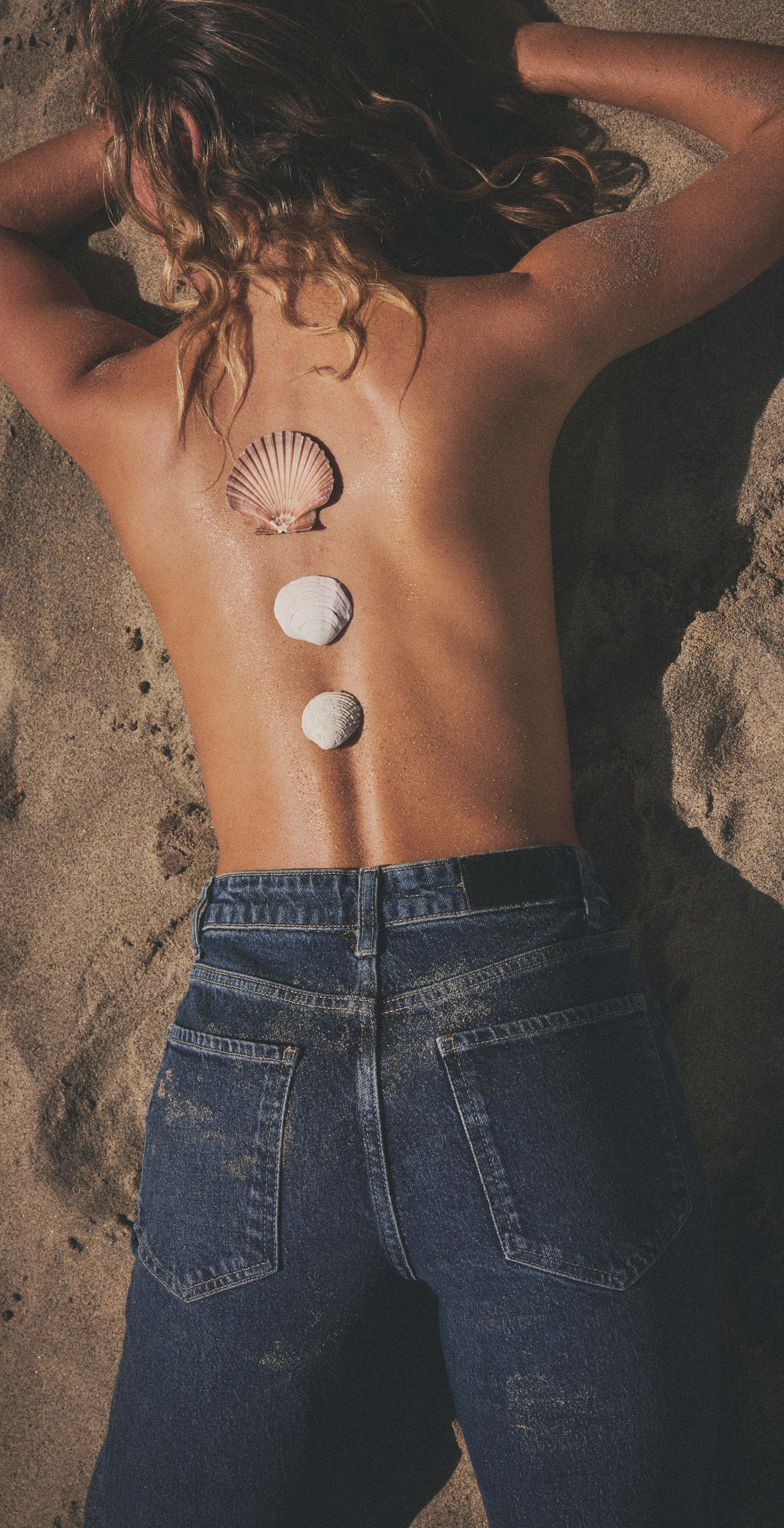 Person lying on sand with three seashells on their back