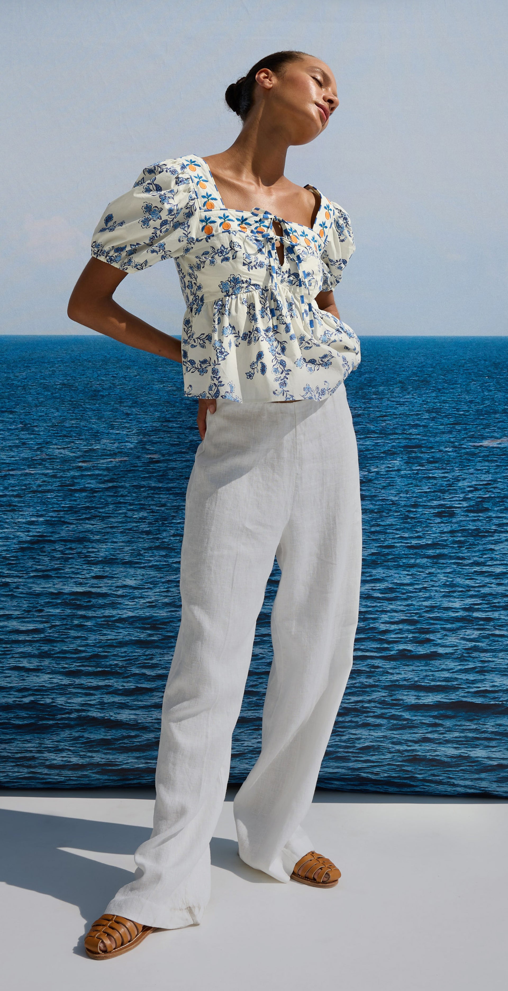 Woman wearing a floral blouse and white pants by the ocean