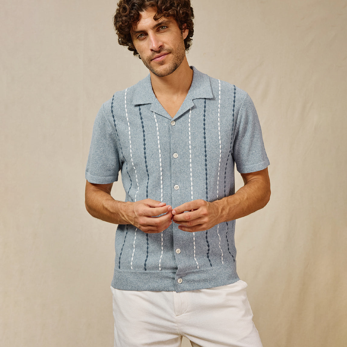 Man wearing a light blue short-sleeve shirt with white patterns on a beige background