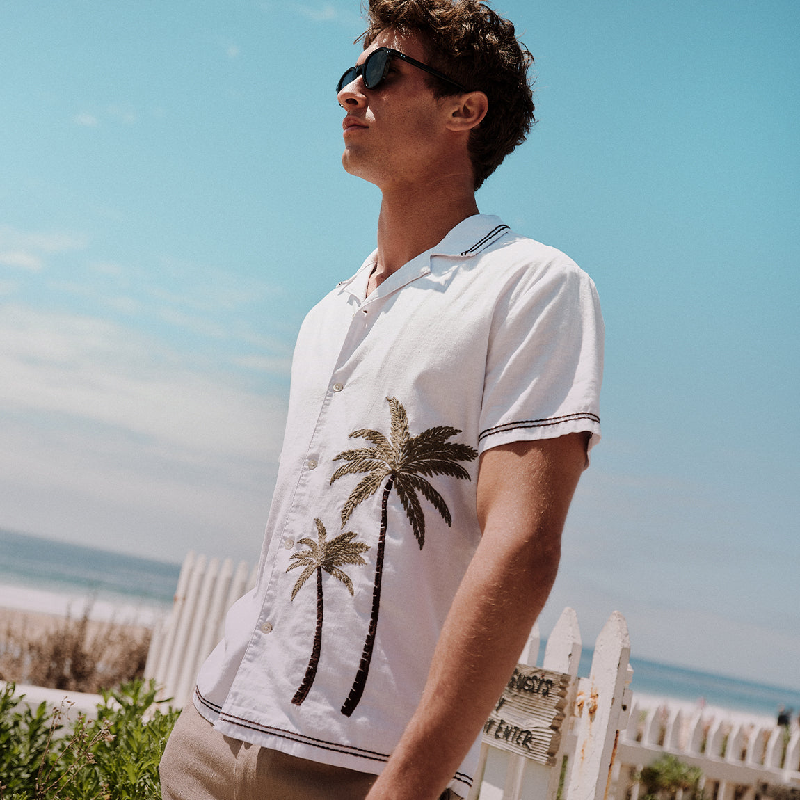 Man wearing a white shirt with palm tree designs on a beach