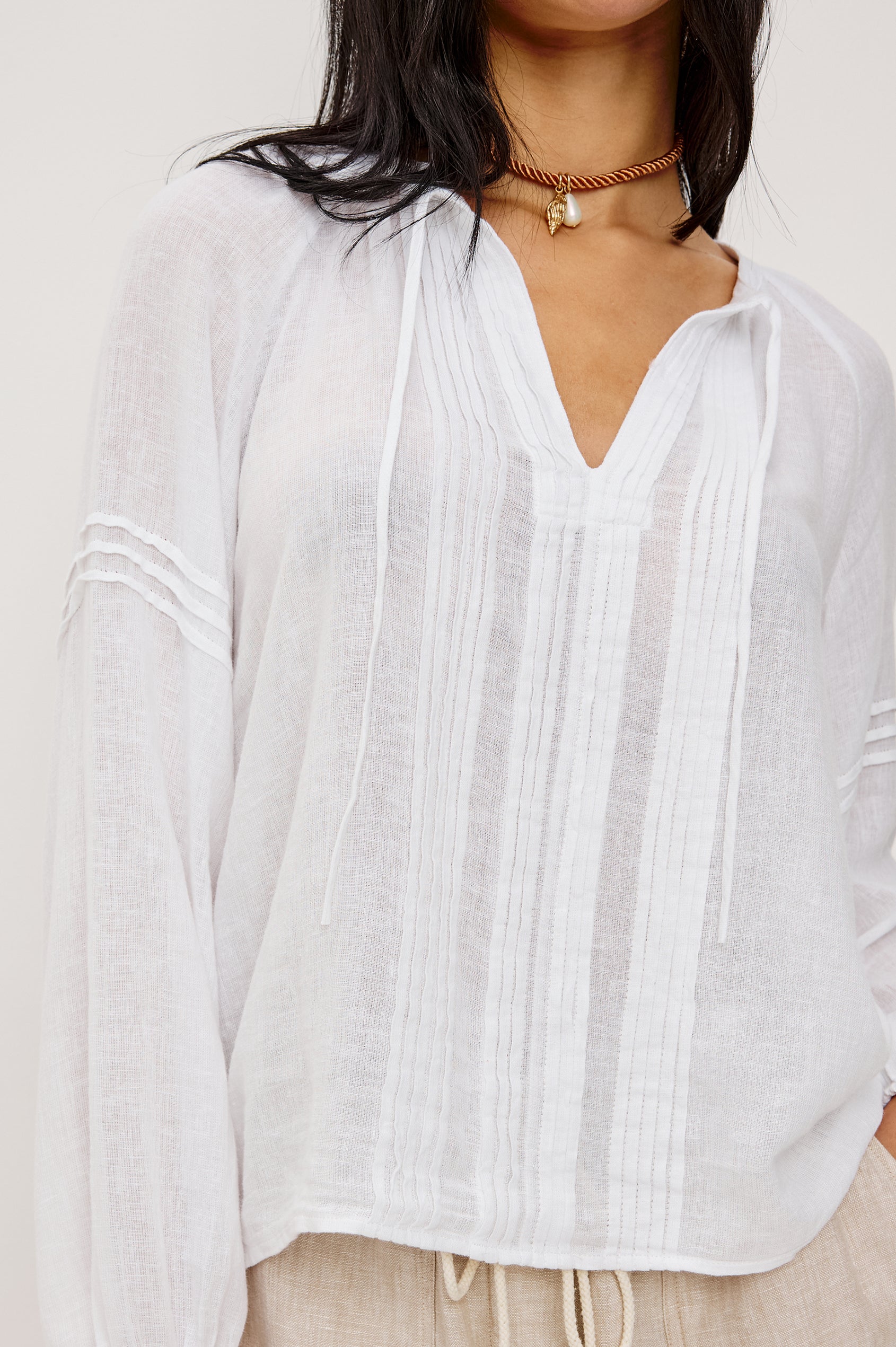 Naples Top in Linen With Split V-Neckline With Self-Ties Long Billowing Sleeves With Fitted Cuffs Loose SIlhouettes and Intricate Seam Detailing in White Colorway - Upper Body Close Up Front View Featured on Model