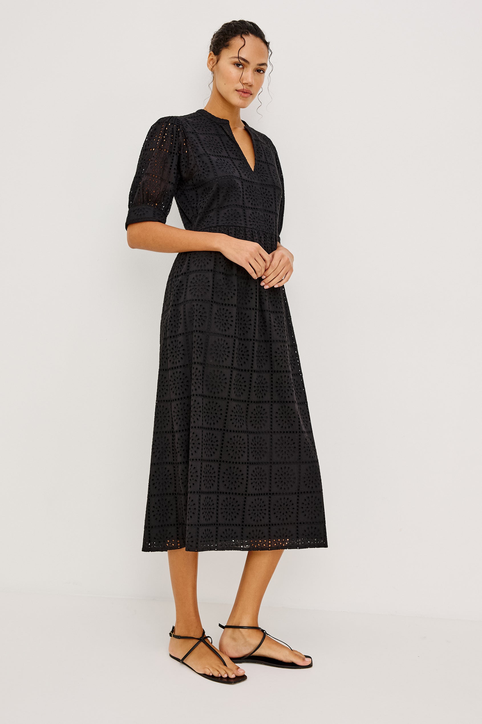 Nella Smock Maxi Dress in Cotton With Grid Eyelet Embroidery Lined Body Split Band V-Neckline Drop Waist Gathered Skirt and Short Puff Sleeves With Fitted Cuffs in Black Colorway - Full Body Front View Featured on Model