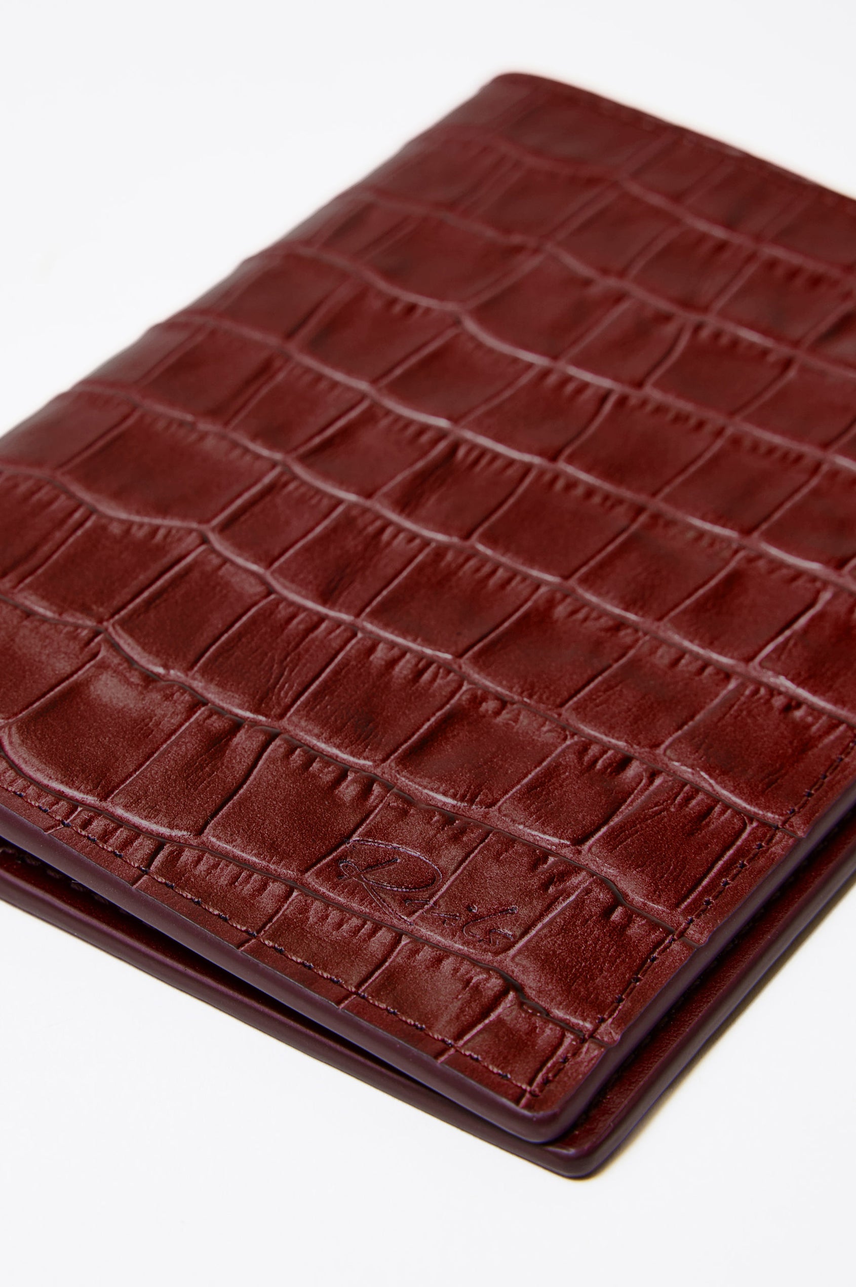 Passport Holder in Croc-Embossed Spanish Leather With Five Card Slots, Two Side Pockets, and Embossed Rails Logo in Burgundy Croc Embossed Colorway - Front close-up flatlay view featured.