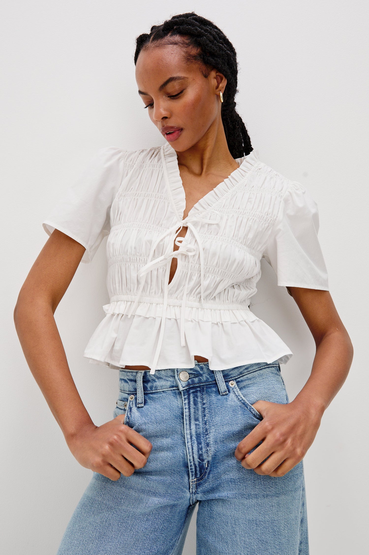 Portia V-Neck Tie Front Top with Short Puff Sleeves and a Ruffled Peplum Hem in White Colorway. Front View Shown on Model looking down.